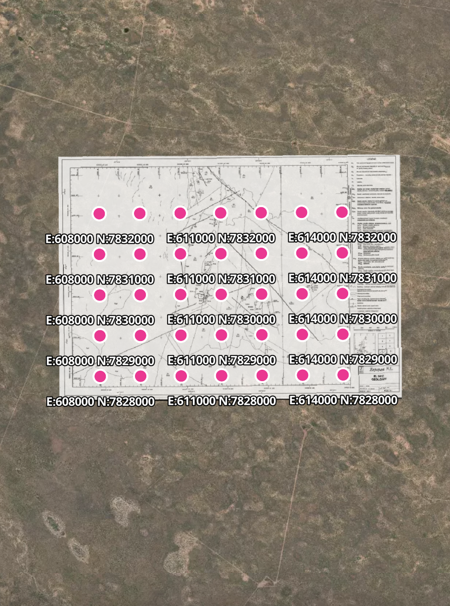 Aerial view of a construction or survey site with a blueprint laid on the ground. The blueprint has pink dots marked with coordinates like E:608000 N:7832000 and others, indicating specific survey points. The area surrounding the blueprint appears to be barren land.