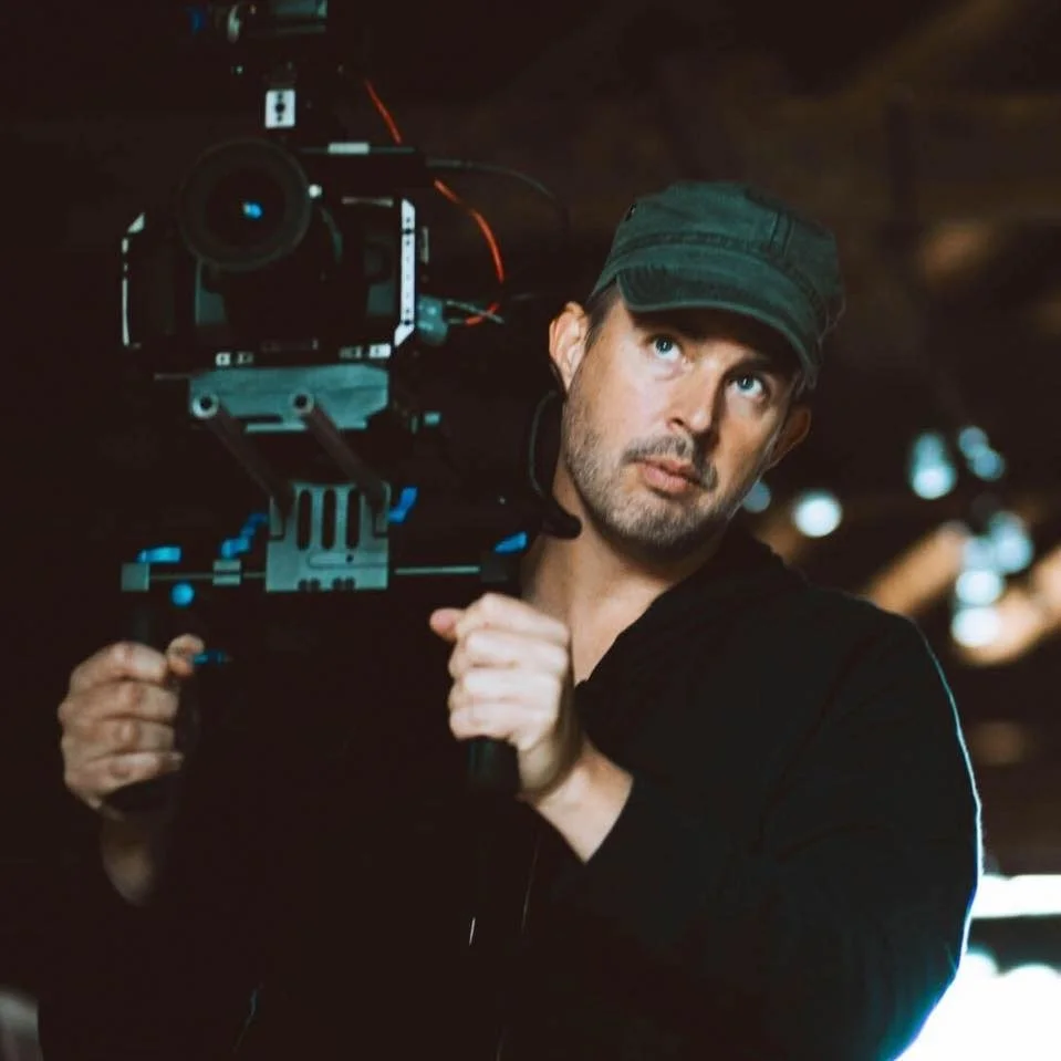 A man with a beard and a cap operating a professional camera in a dark environment.