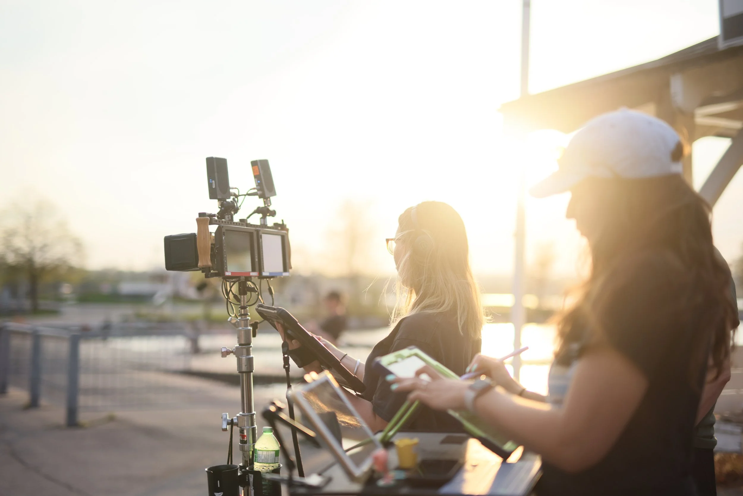People working on a film set outdoors during sunset, with a camera and electronic devices.