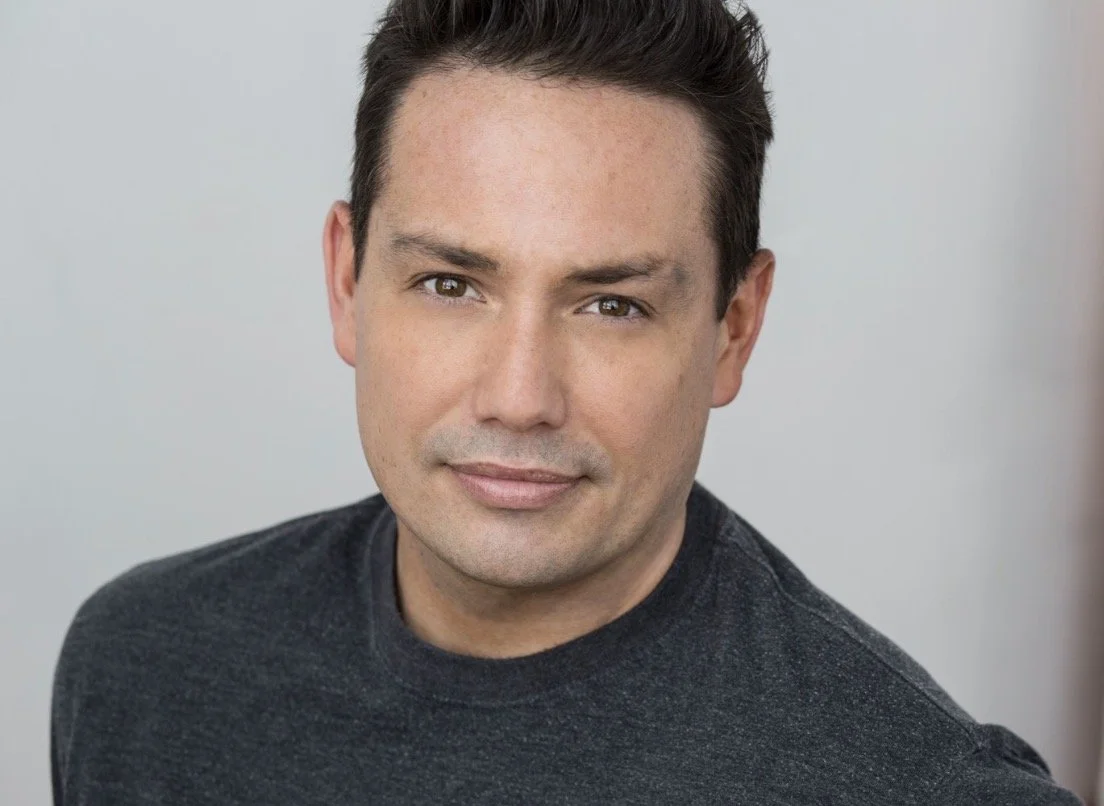 Headshot of a man with short dark hair, wearing a dark gray shirt, looking directly at the camera with a neutral expression.