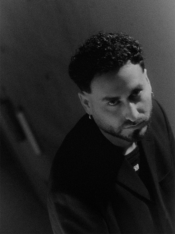 Black and white photo of a man with curly hair and a beard, looking up at the camera with a serious expression.