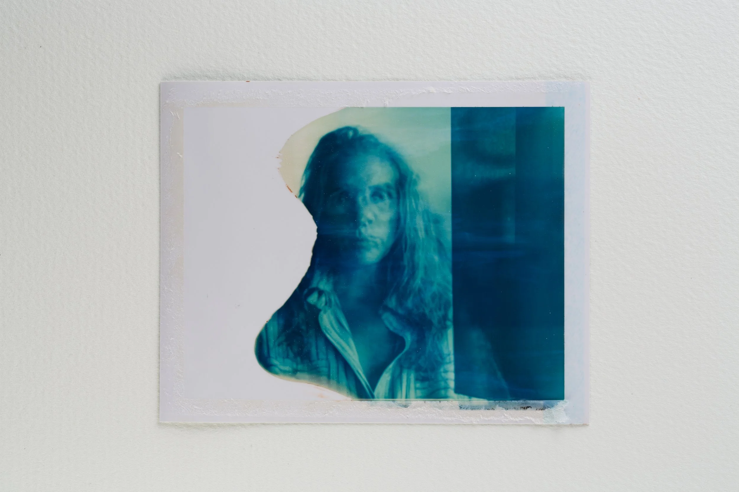 A portrait of a woman with long hair, with part of the image blurred and distorted, mounted on a white wall.