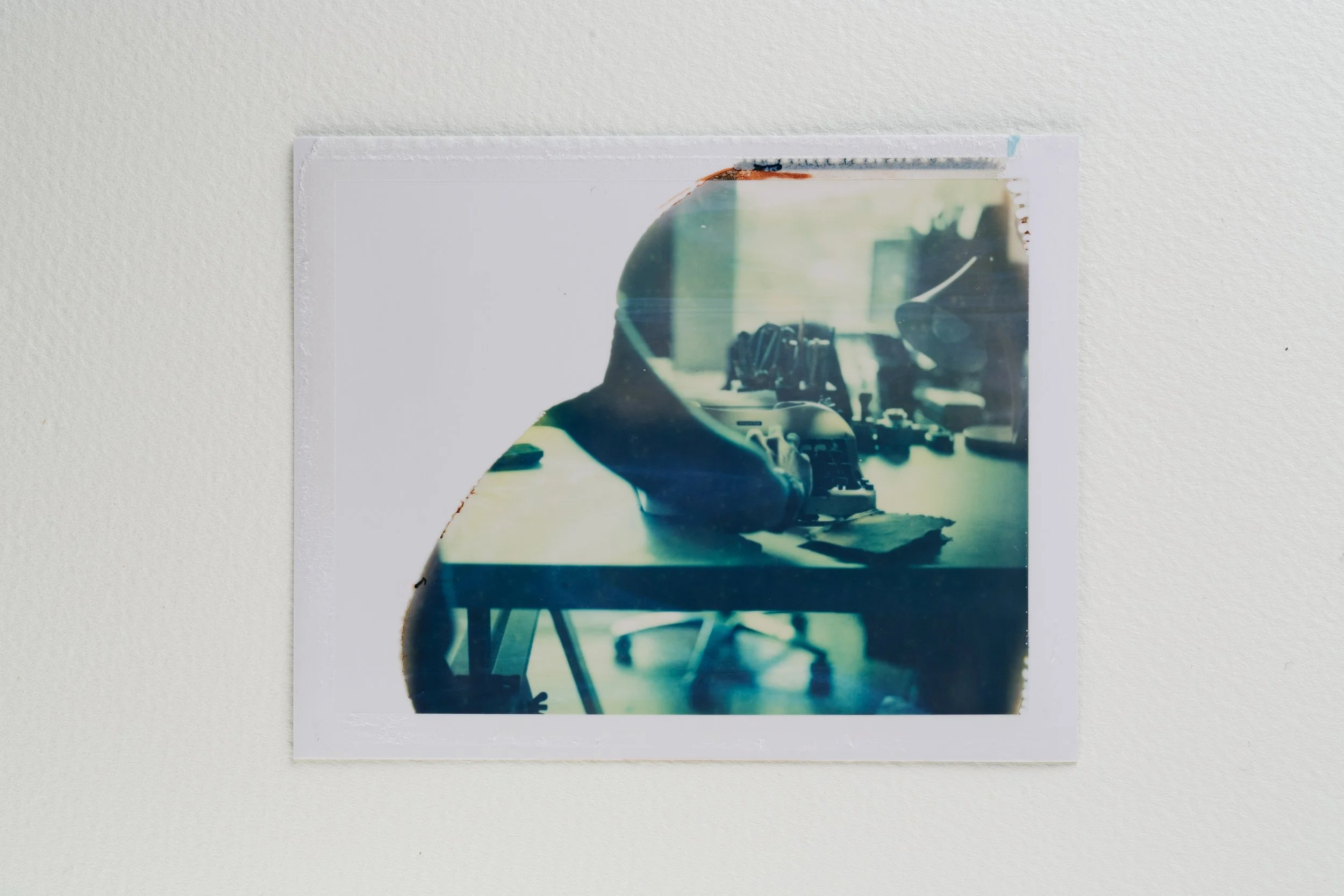 A printed photo on a white wall showing a person working on a desk with electronic components, with reflections and a double exposure effect.