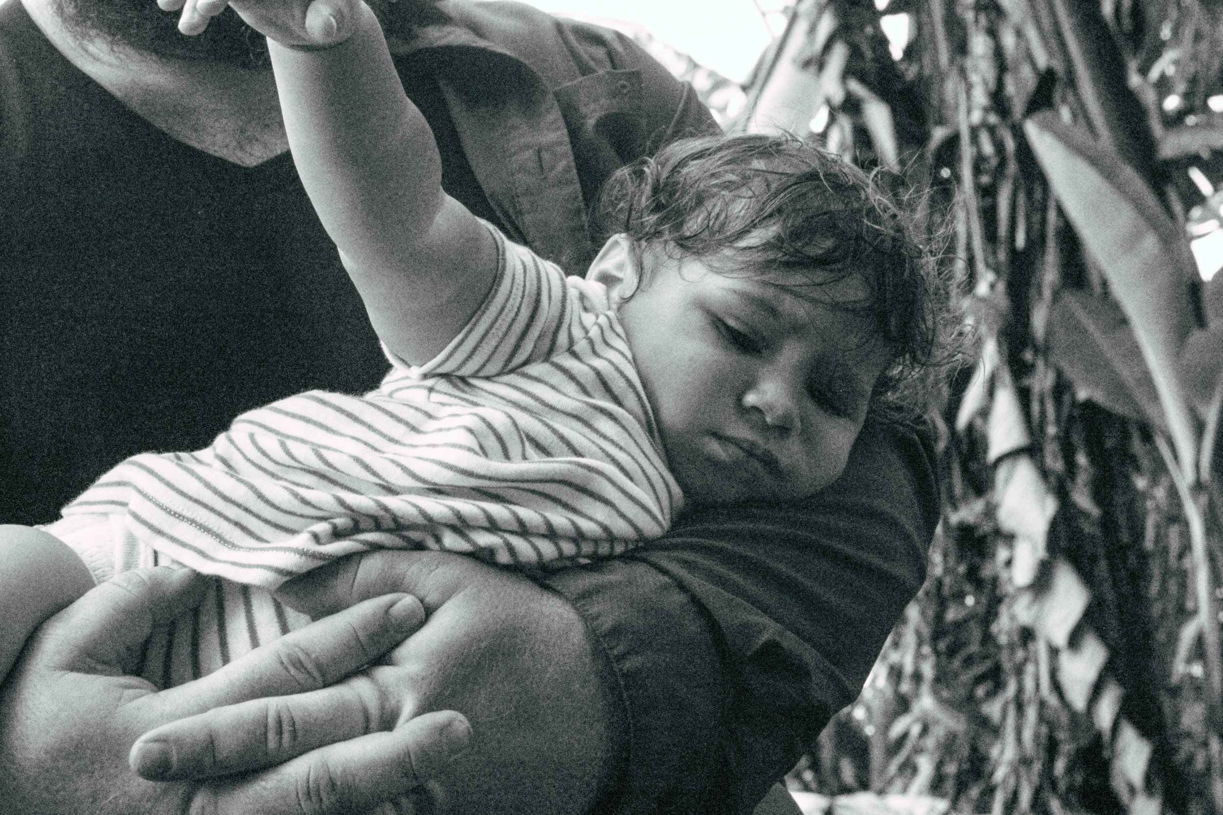 A young child sleeping on an adult's arm, with a background of hanging textiles.