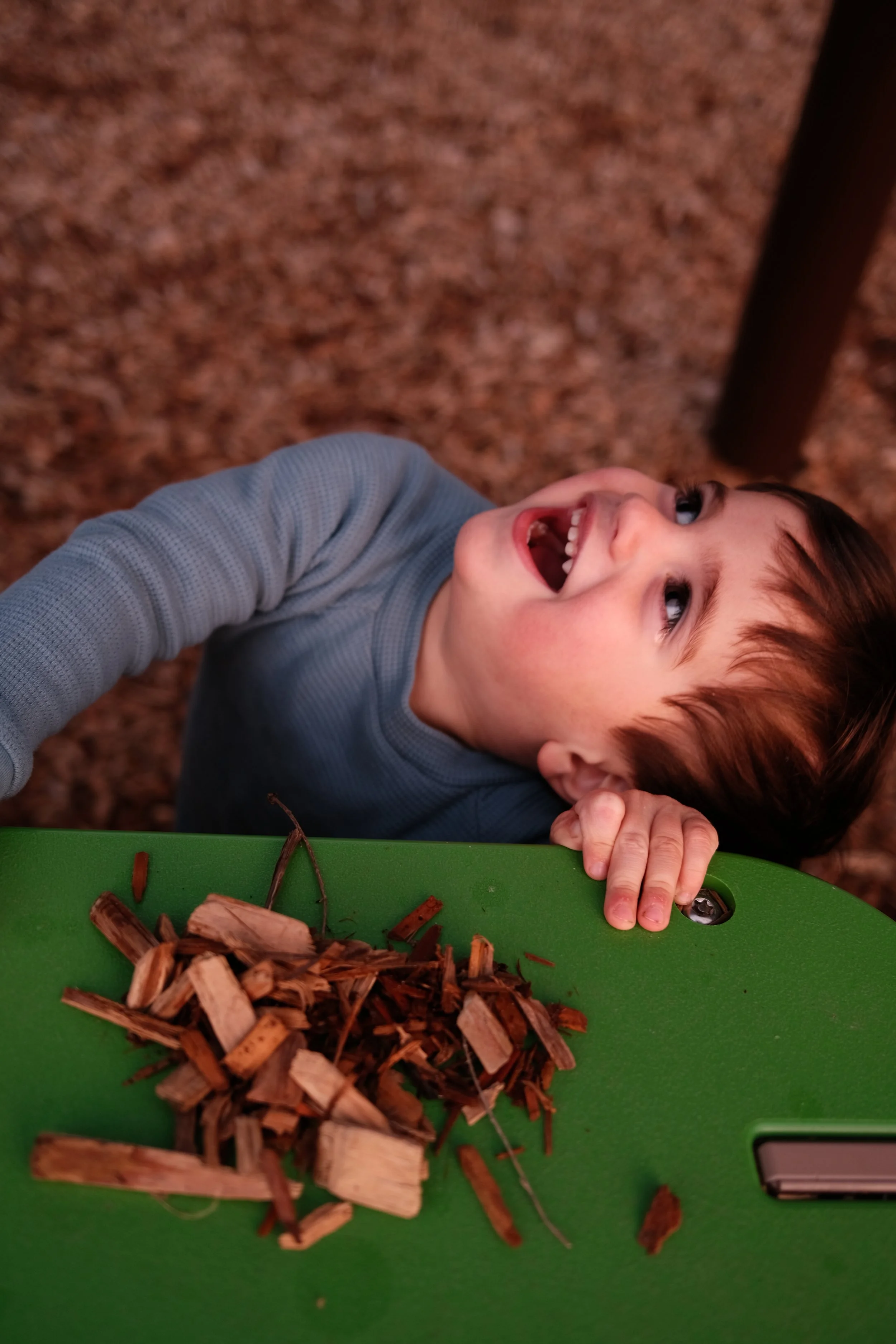 Menino sorridente brincando ao ar livre com madeira no chão.