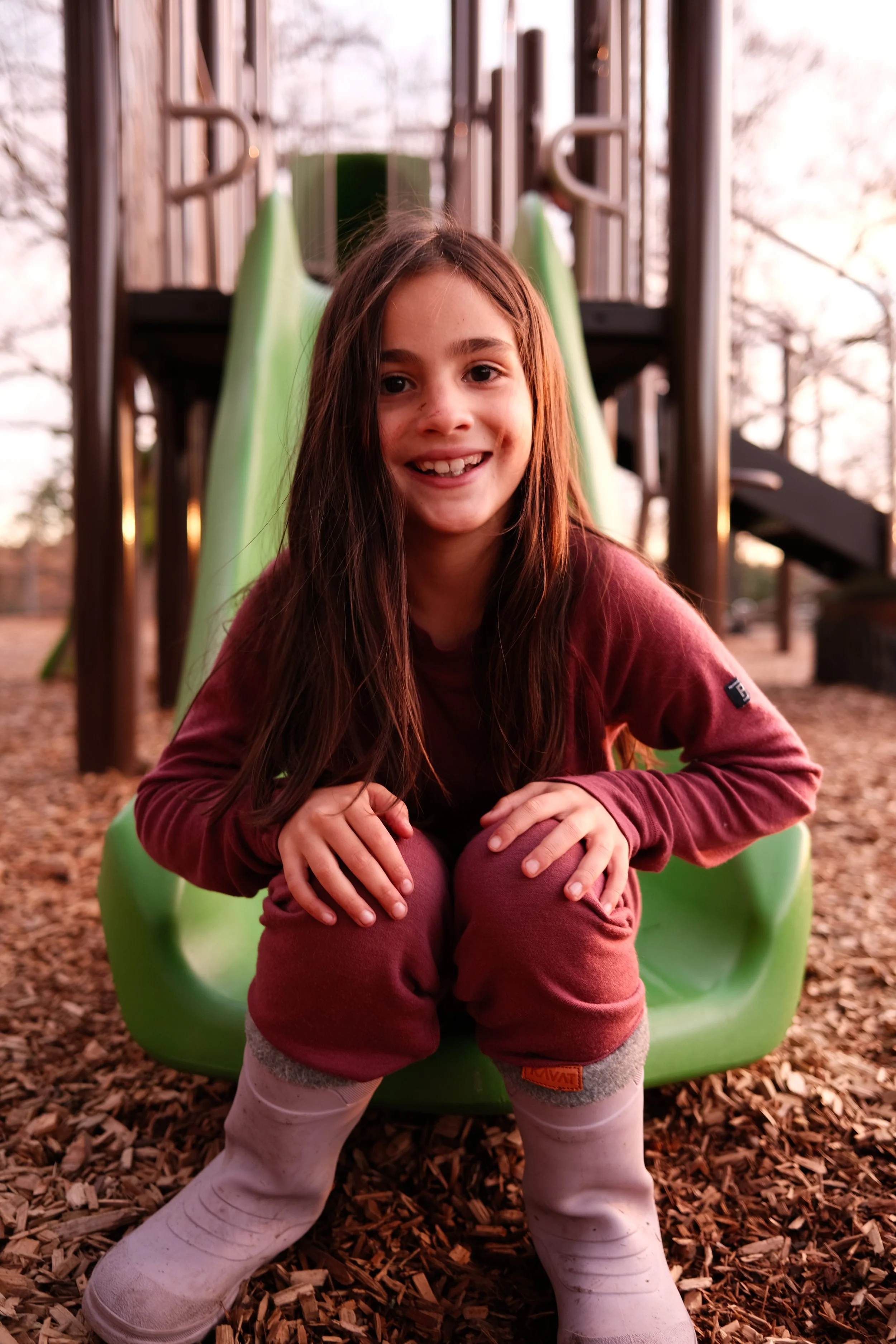 Menina sorridente brincando numa escorregador de parque infantil ao ar livre.