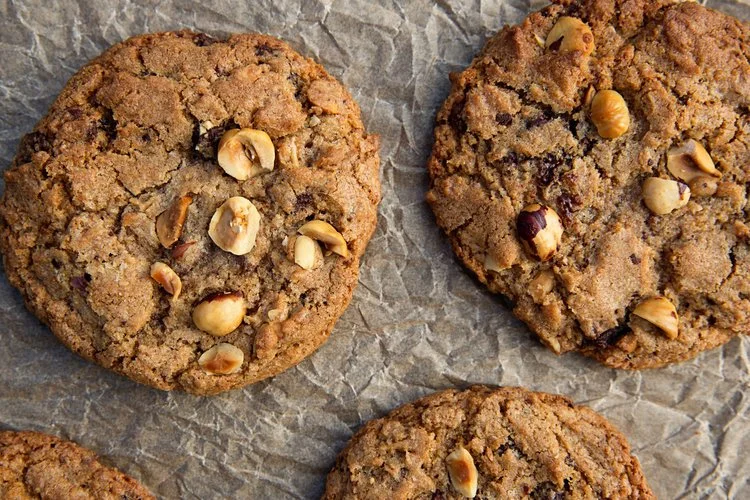 Close-up of three chocolate chip cookies with chopped nuts on a crinkled parchment paper.