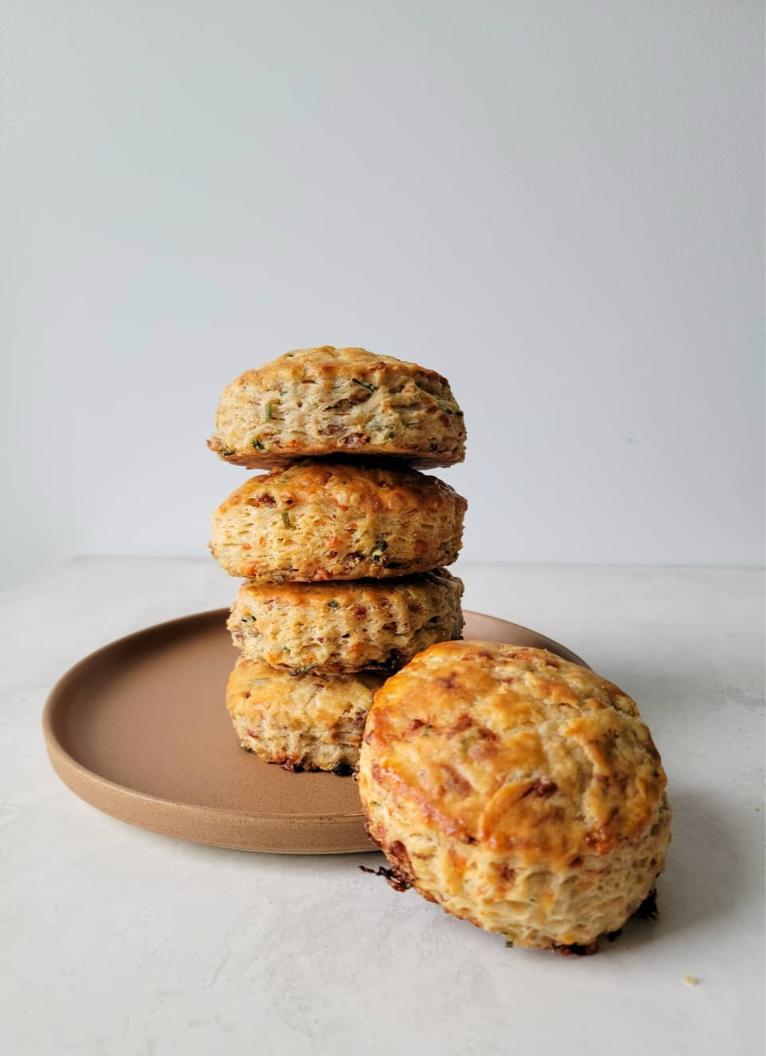 Four scones stacked on a brown plate with one scone leaning against the stack, set on a white surface against a plain light gray background.