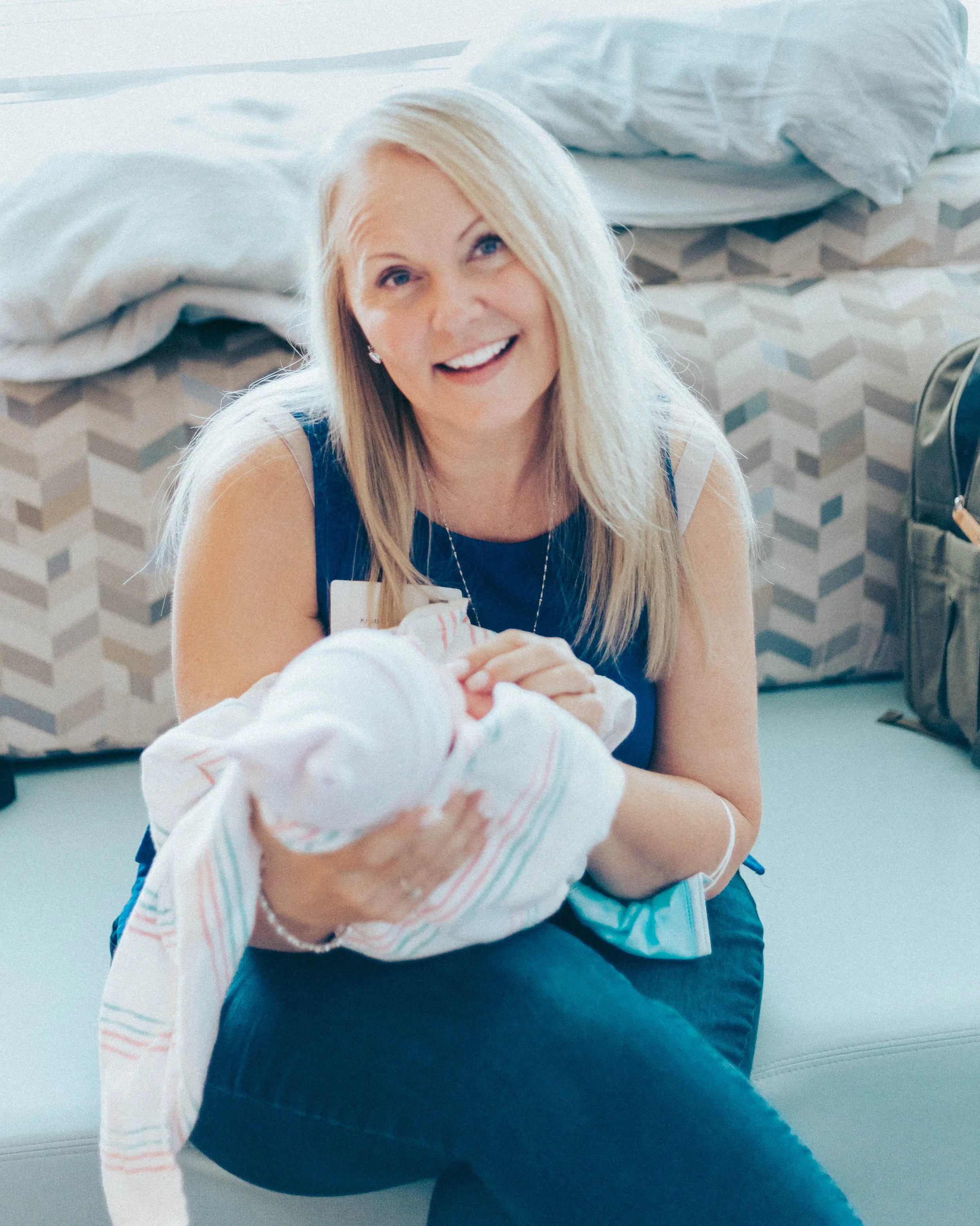 A woman smiling while holding a newborn baby wrapped in a hospital blanket.
