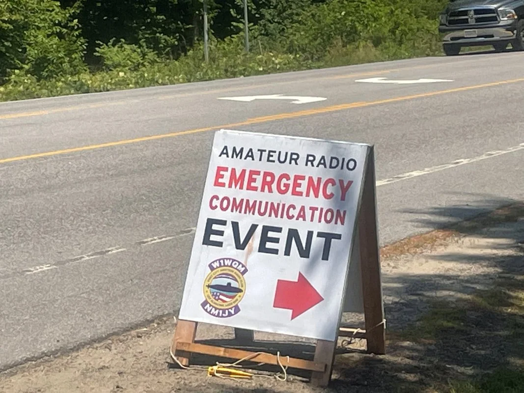 A roadside sign indicating an amateur radio emergency communication event, with an arrow pointing to the right and the town seal for Towim.