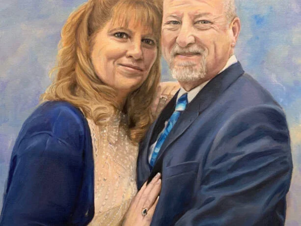 A middle-aged woman with long, wavy blonde hair and a middle-aged man with a beard and short hair posing together, both wearing formal attire, in front of a painted background.