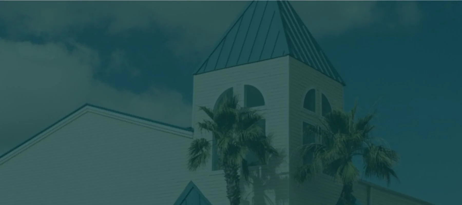 A church with a steeple, beige walls, and arched windows, with palm trees in front, under a partly cloudy sky.