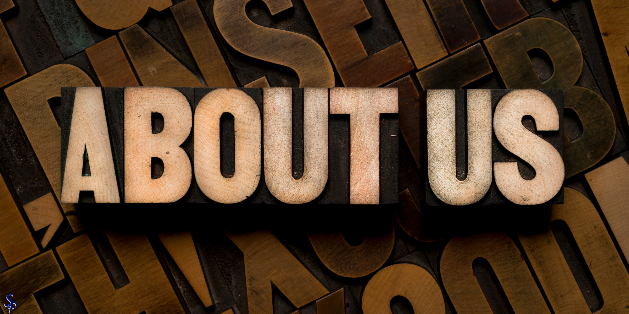 Wooden block letters spelling 'ABOUT US' on a wooden background with scattered letter tiles.