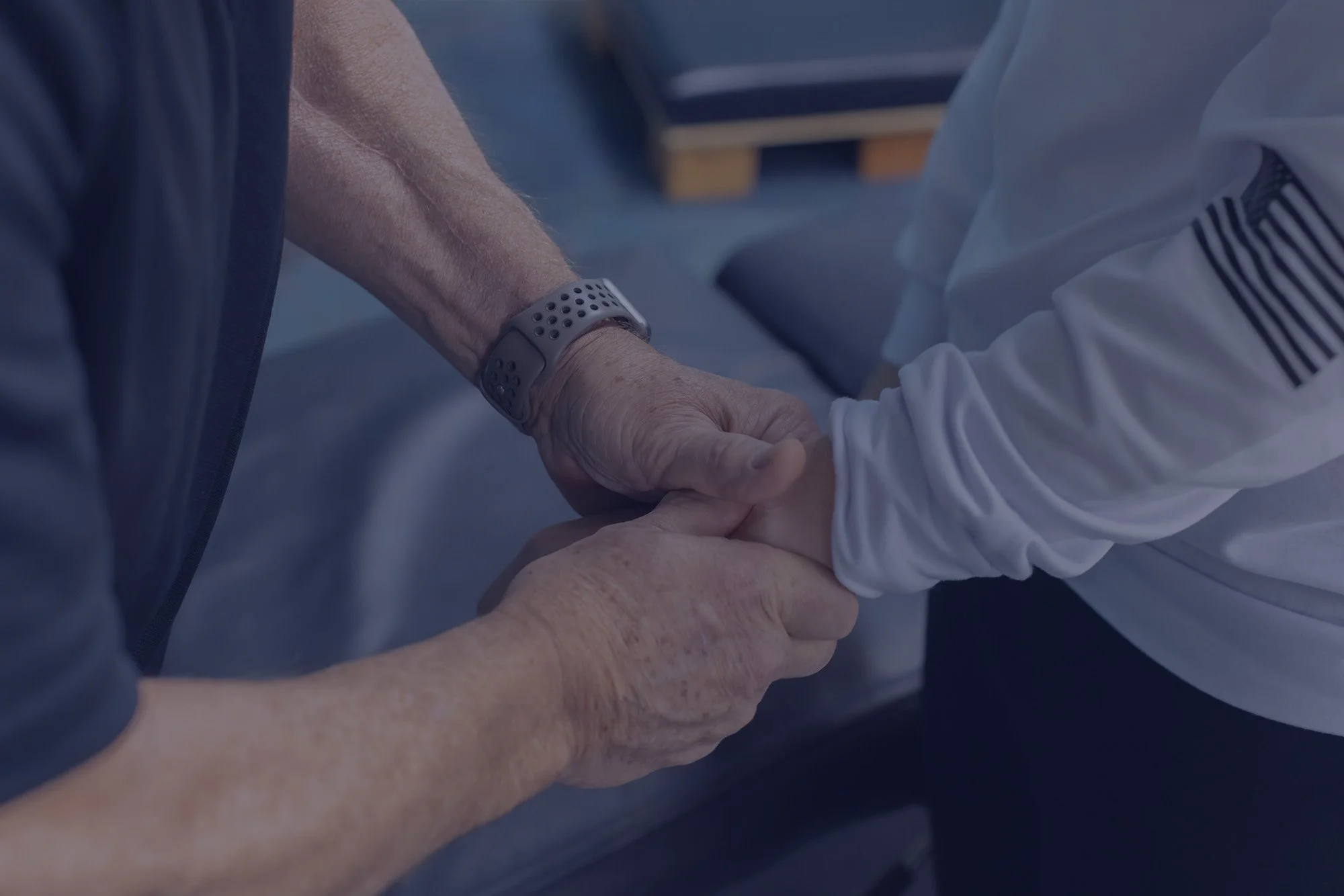 Two people, one elderly and one younger, holding hands in a gesture of support or care.