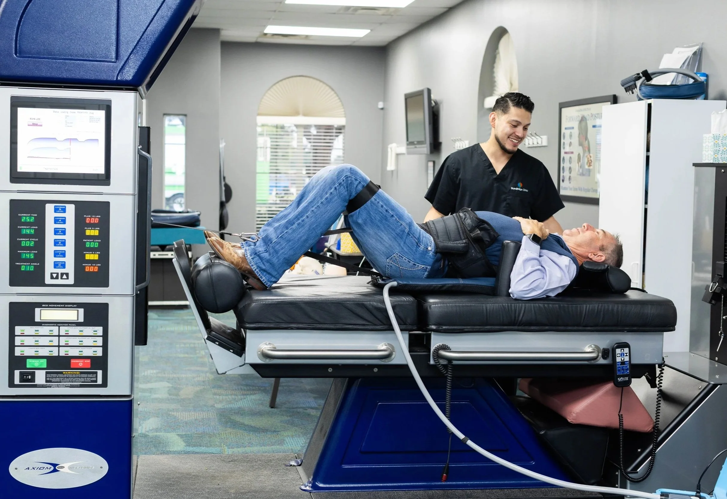 A medical professional demonstrates a spinal decompression treatment on a patient lying on a specialized table in a medical office.