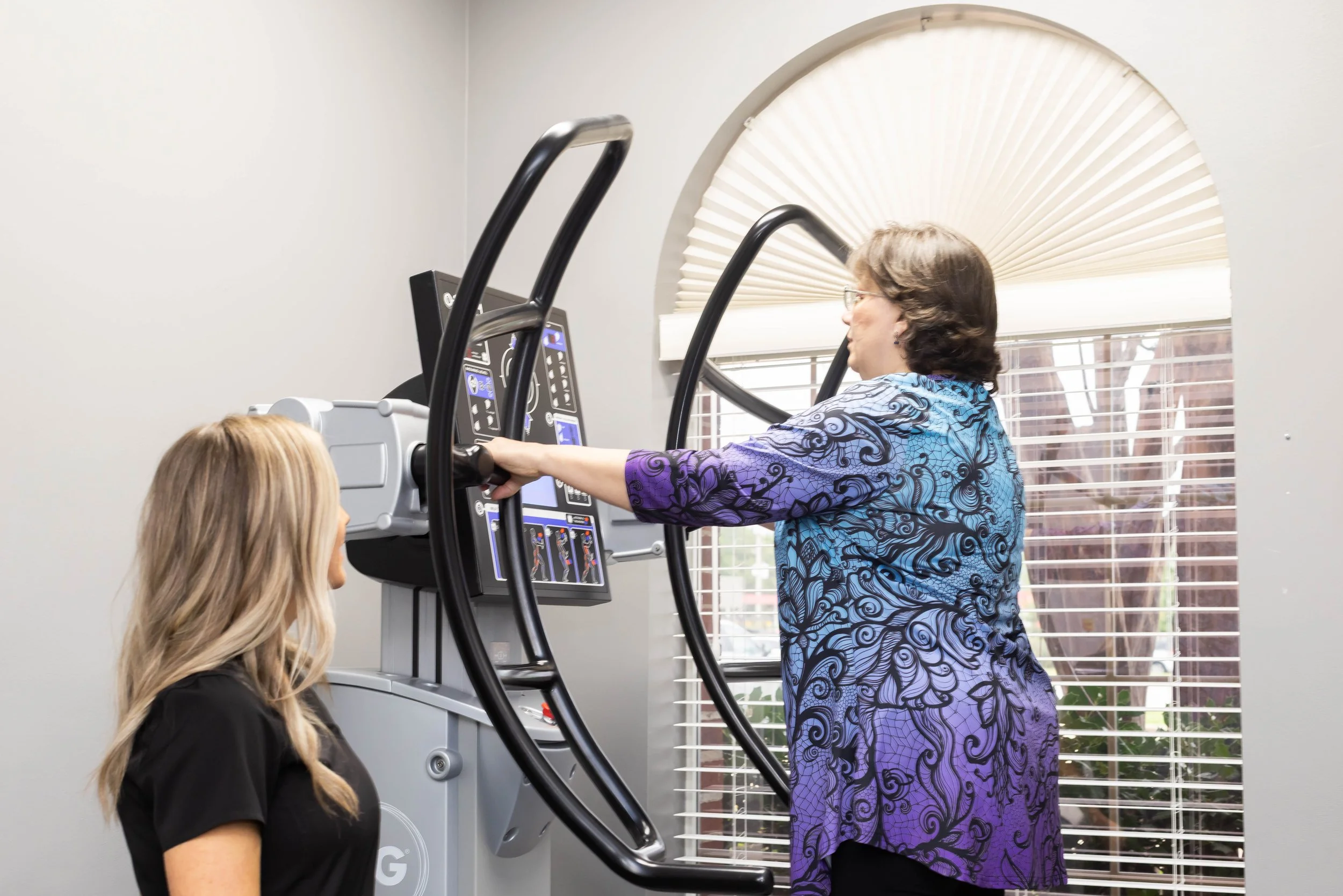 Two women in a medical setting, one using a large, high-tech diagnostic imaging machine with a circular opening, while the other observes.