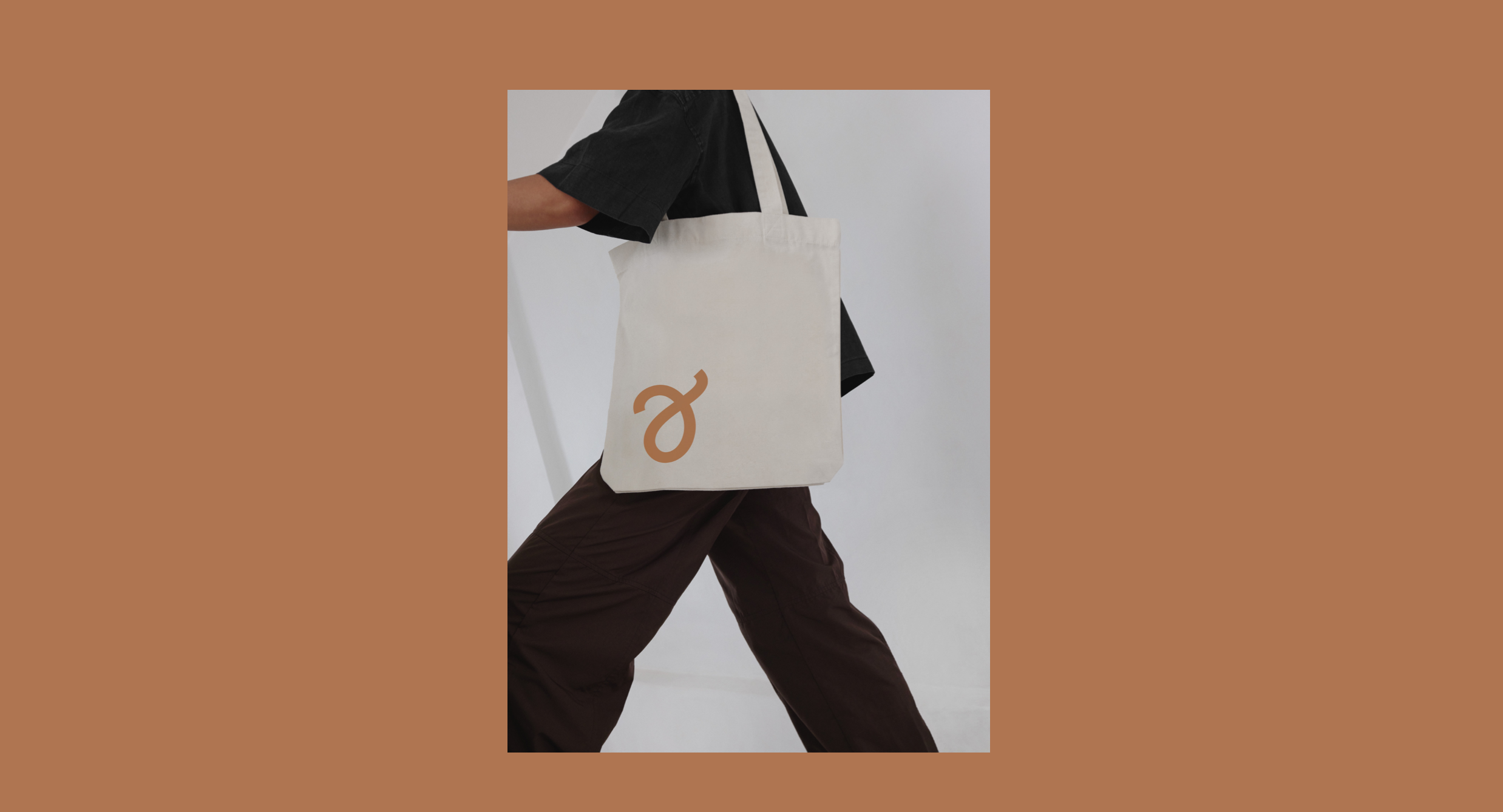 Person som går i mørke klær med en hvit totebag med en brunt logo.
