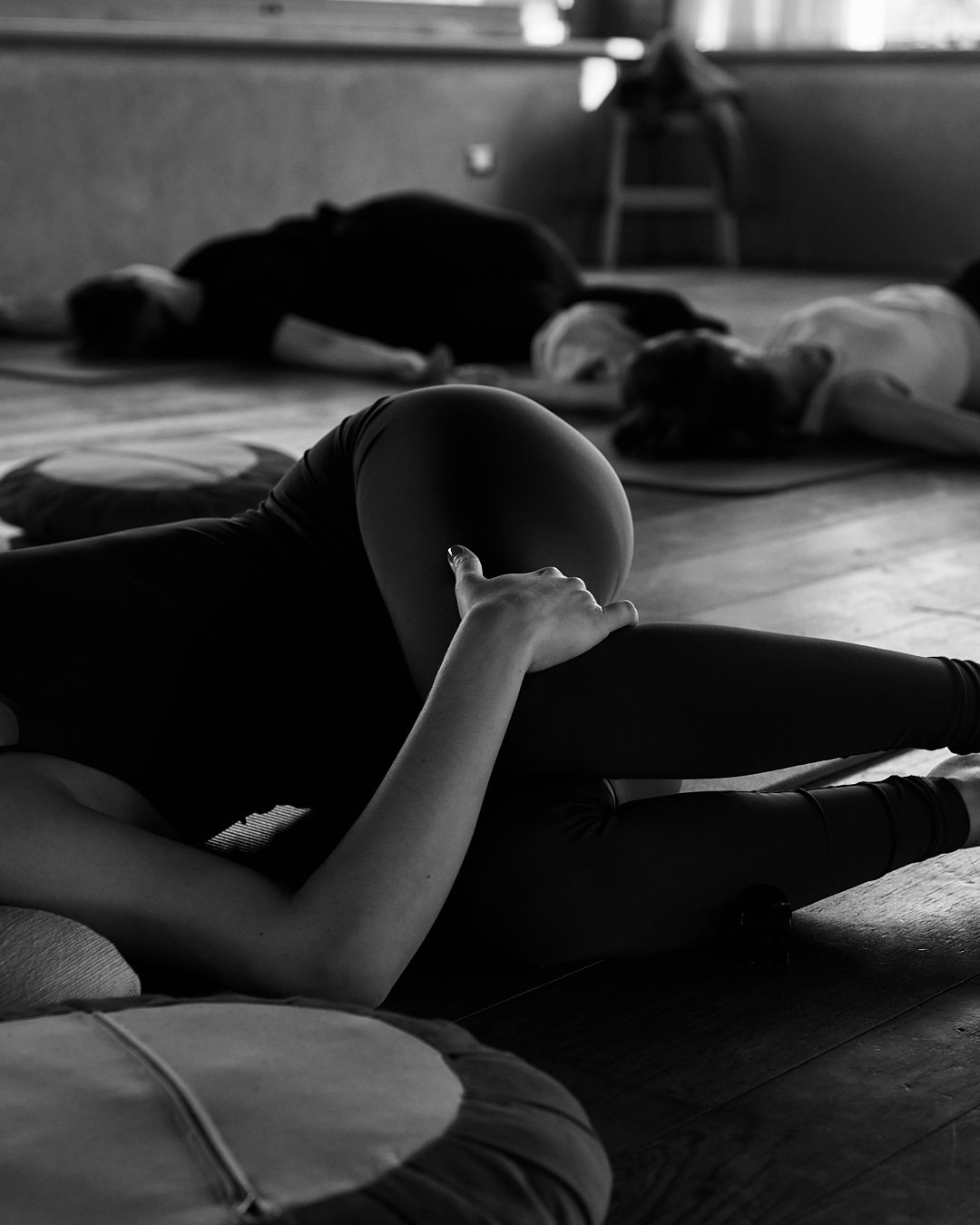 Persone che praticano yoga o meditazione in una stanza, distese a terra su tappetini.