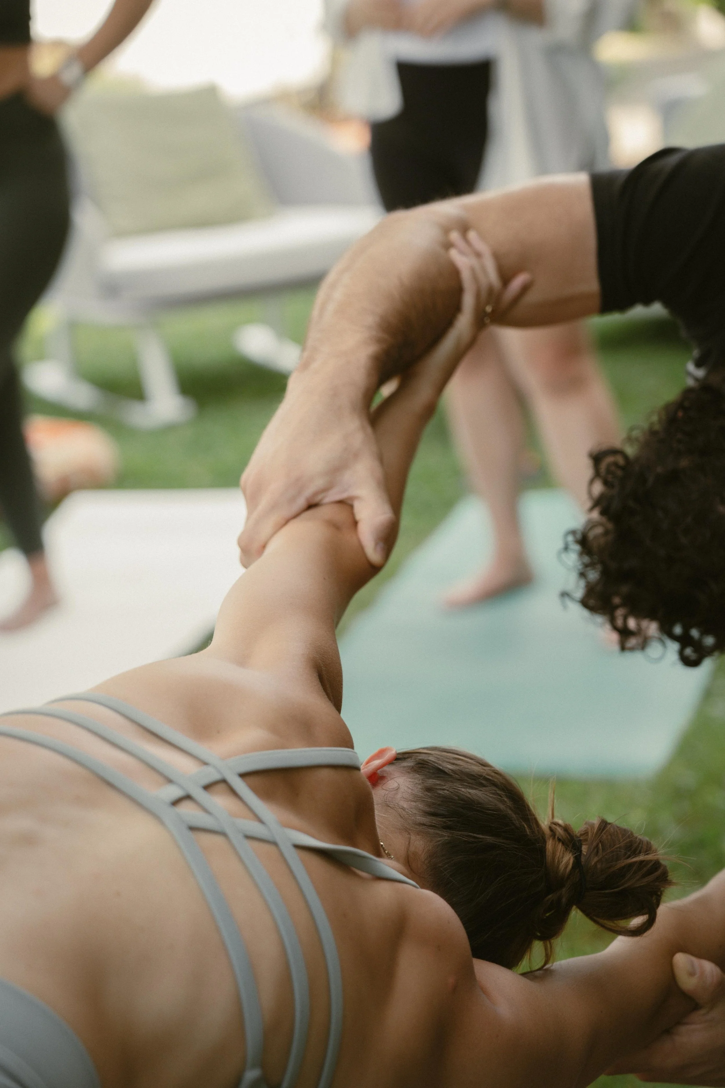 Due persone che praticano yoga o stretching in un ambiente interno, con un'altra persona in piedi in background.