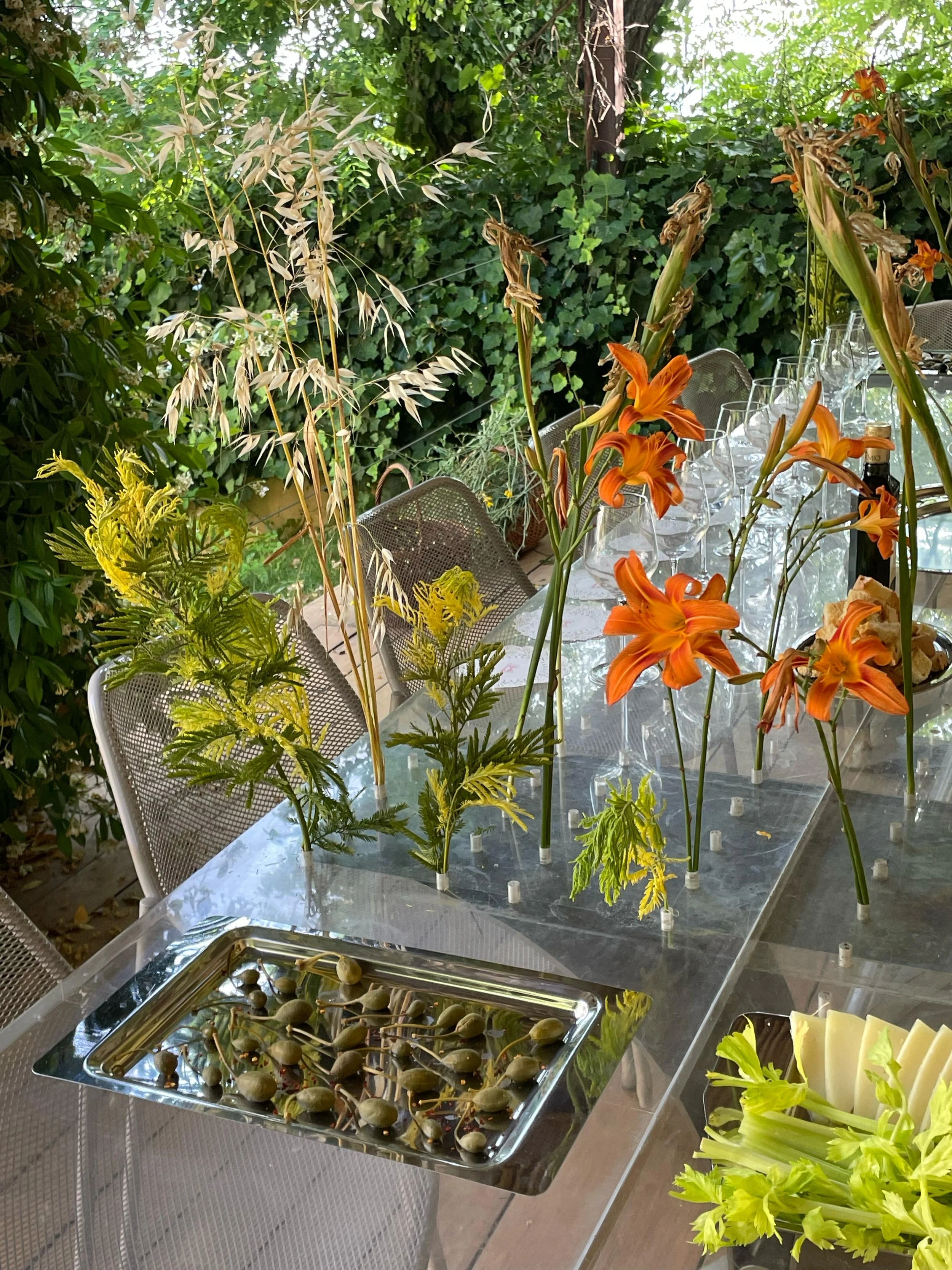 Tavolo con decorazioni floreali arancioni e verdi, e cibo con uva in una tavola da pranzo all'aperto circondata da piante.