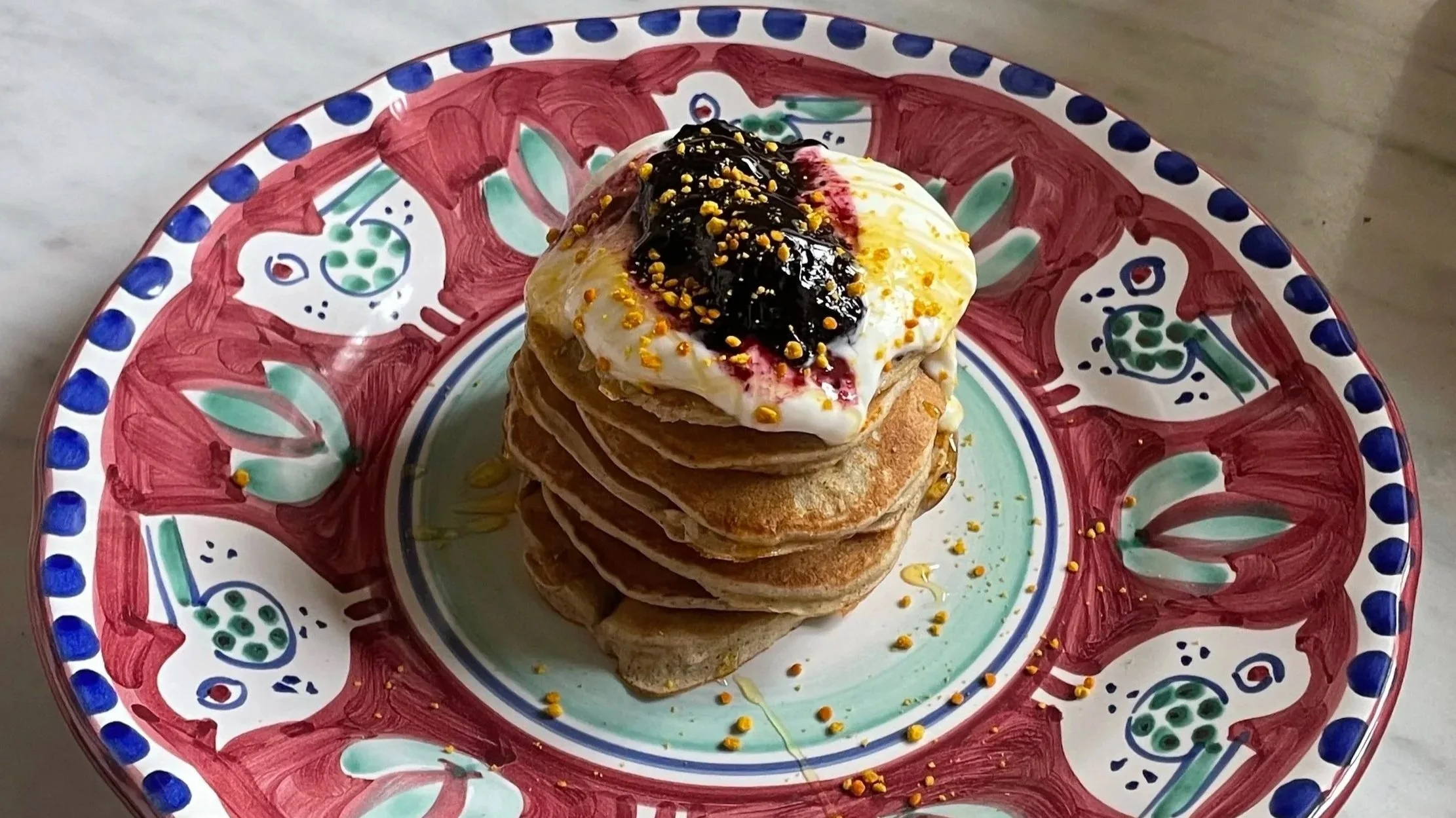 Piatto di pancakes con zucchero a velo, sciroppo di mirtillo e granella di giallo