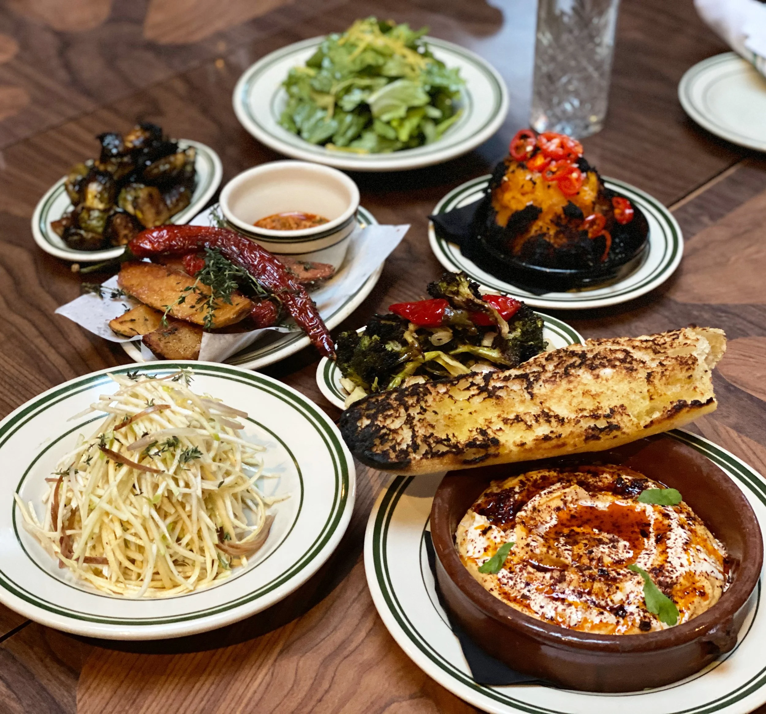  assortment of Indian dishes on a wooden table, including papadum, chana masala, paneer, grilled vegetables, salad, and various curries with garnishes and spices.
