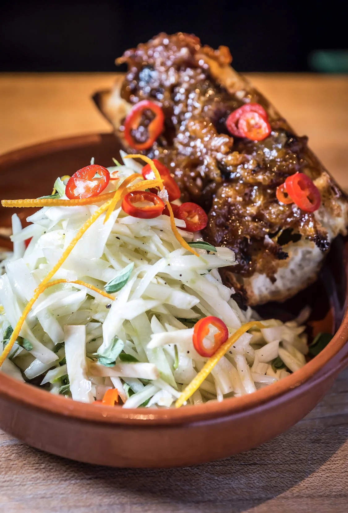 A serving of barbecue ribs with a side of coleslaw topped with sliced red chili peppers and shredded lemon peel.