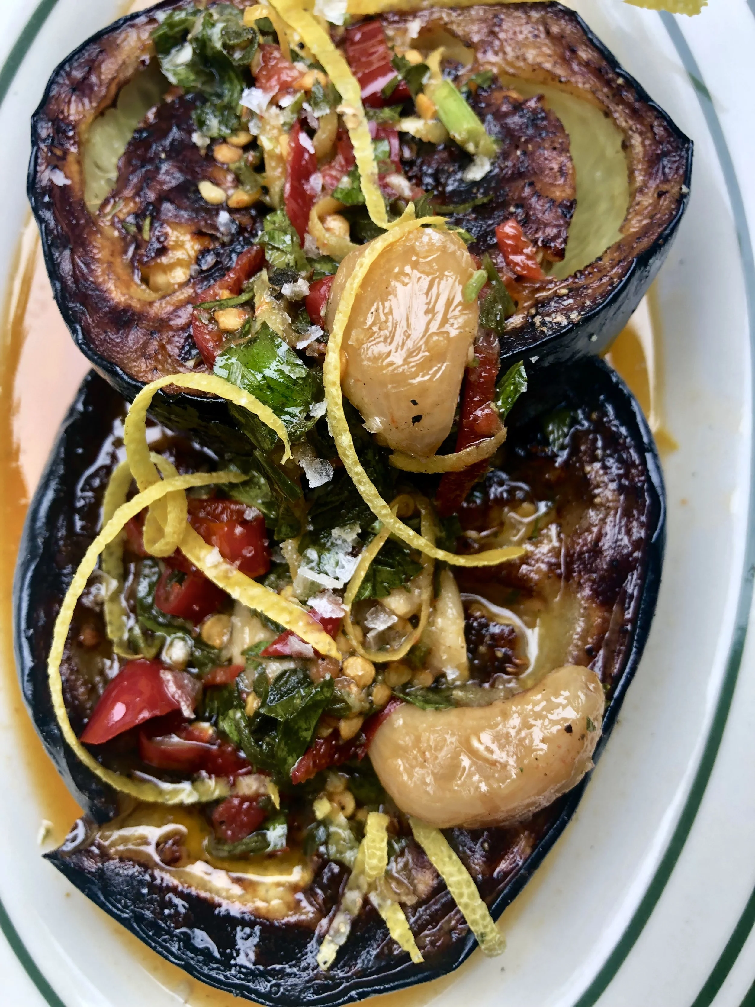 Two grilled eggplant halves topped with chopped tomatoes, green herbs, lemon zest, and pine nuts.