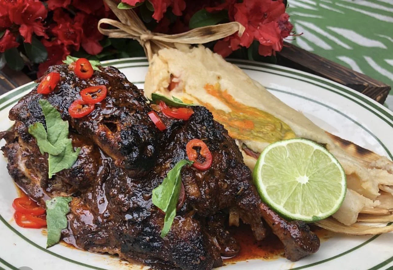 Barbecue ribs with red chili slices and fresh basil on a white plate, accompanied by a slice of lime and a baked potato with cheese and vegetables.