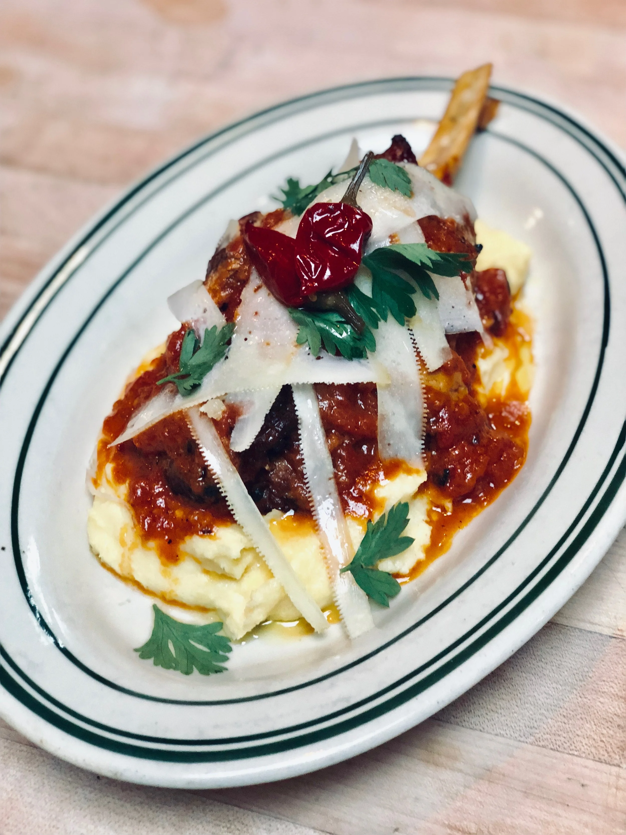 A plate of loaded mashed potatoes topped with chili, shredded cheese, cilantro, and a red chili pepper.