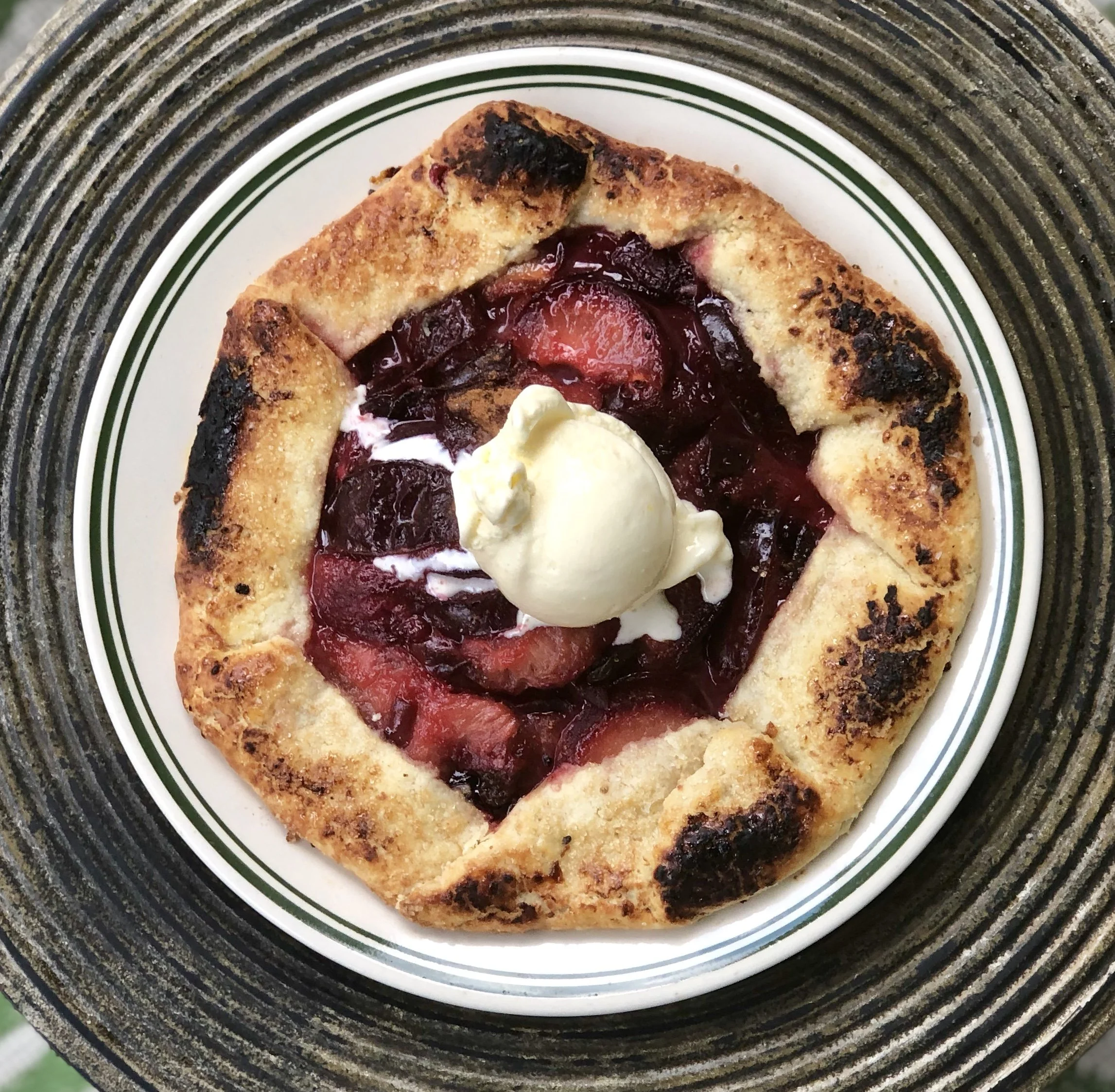 A circular fruit galette with a golden, flaky crust, filled with a mixture of chopped berries and sliced strawberries, topped with a scoop of vanilla ice cream.