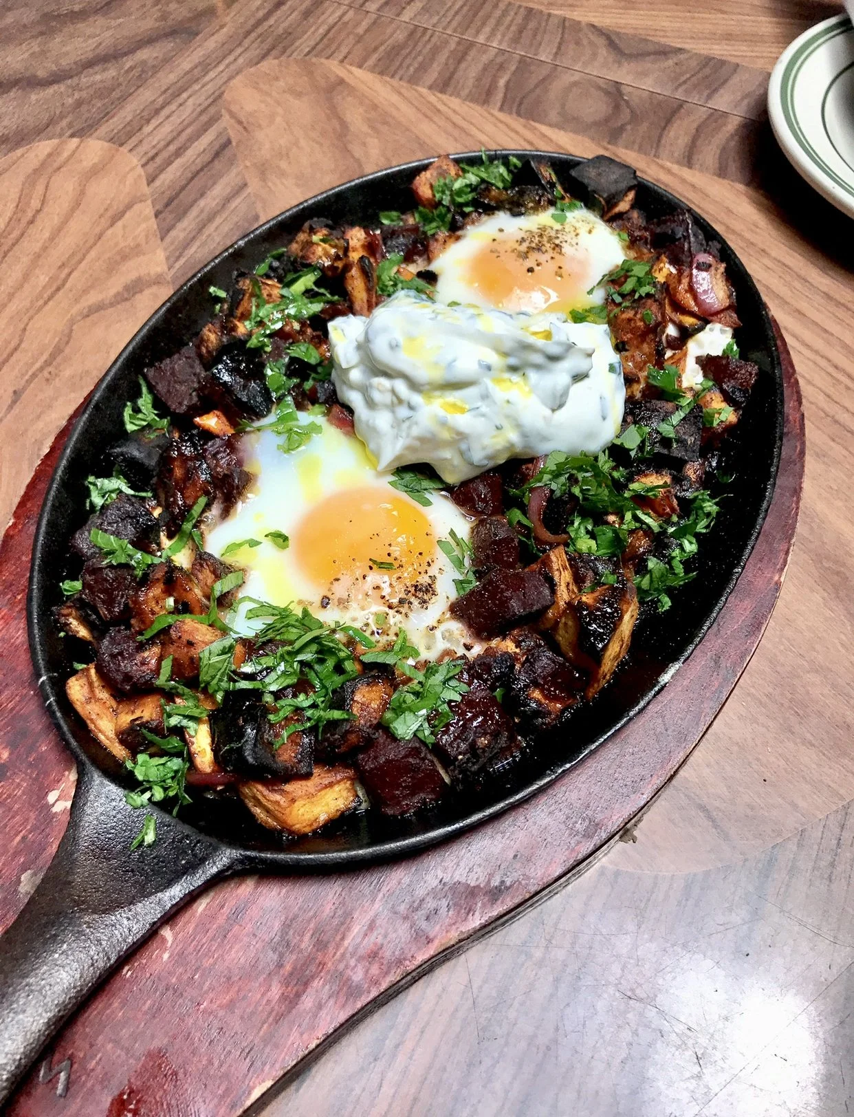 Skillet of seasoned roasted vegetables topped with two poached eggs, garnished with chopped parsley and a dollop of sour cream or yogurt.