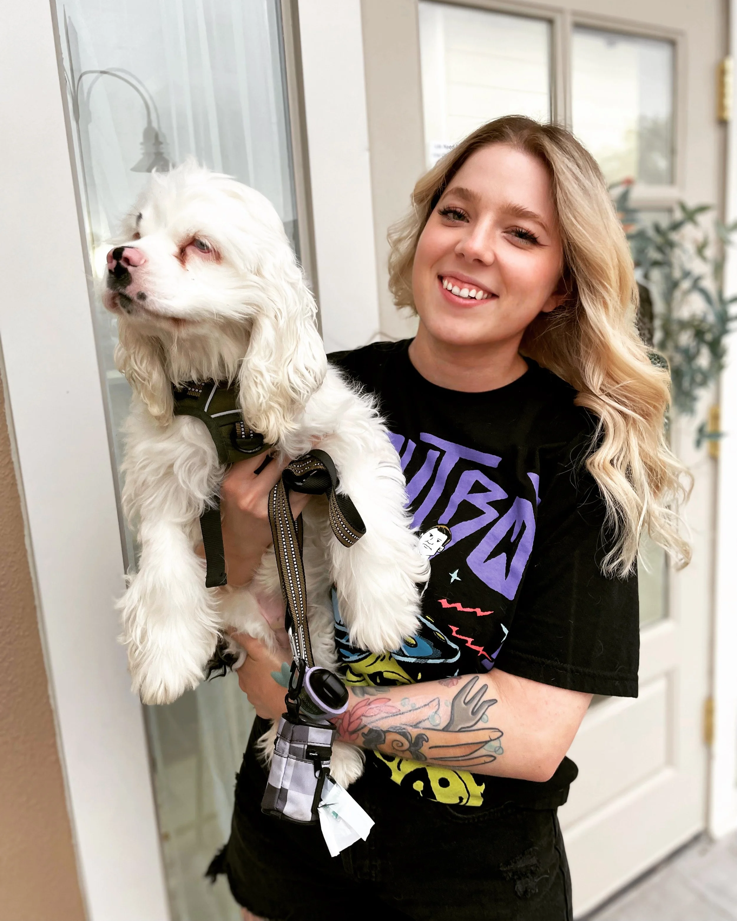 A smiling woman with blonde hair holding a white dog with floppy ears outside a store.