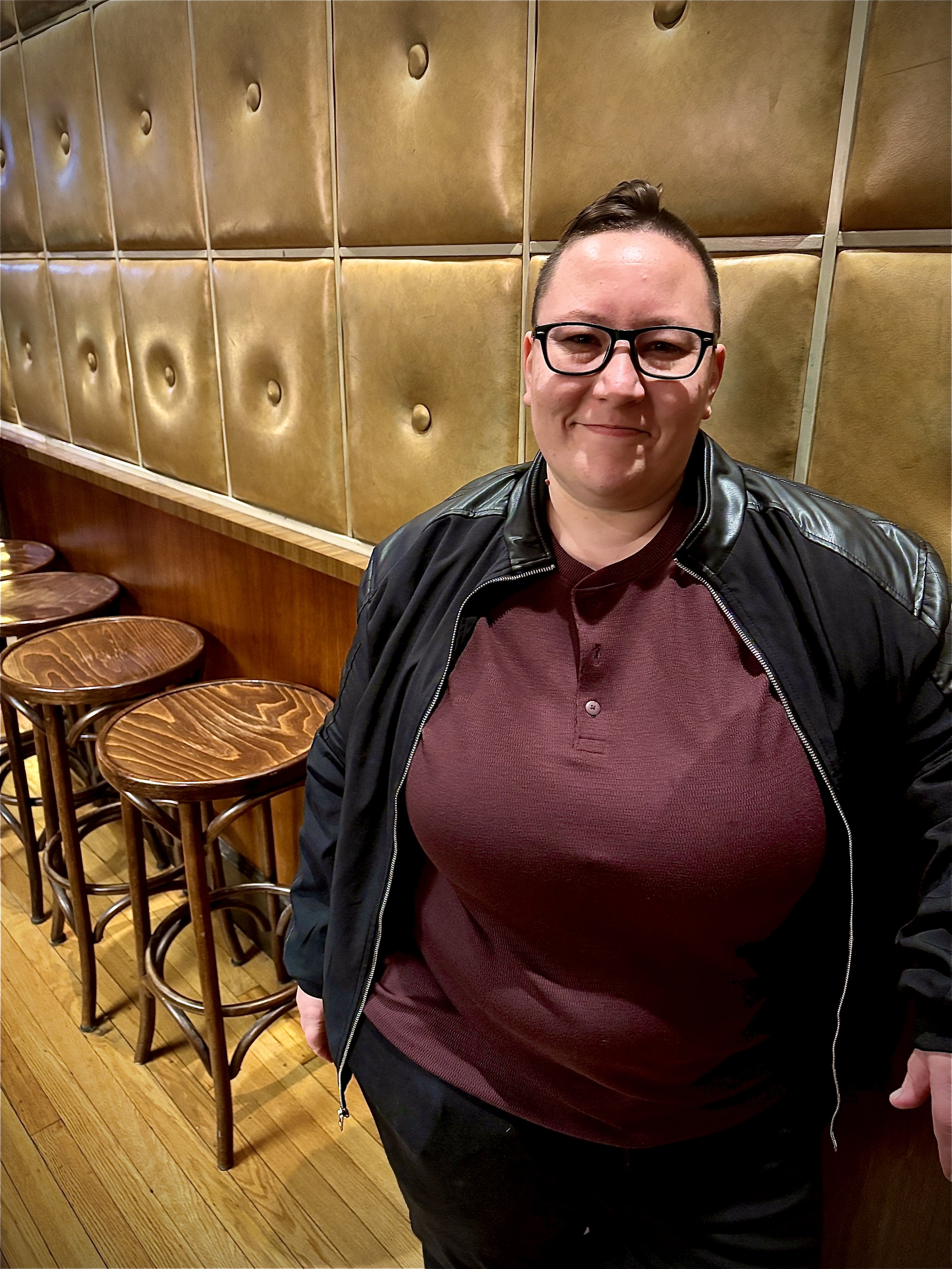 Mx. Asher standing near a bar at the Monthly Musings Open Mic where they were a featured performer