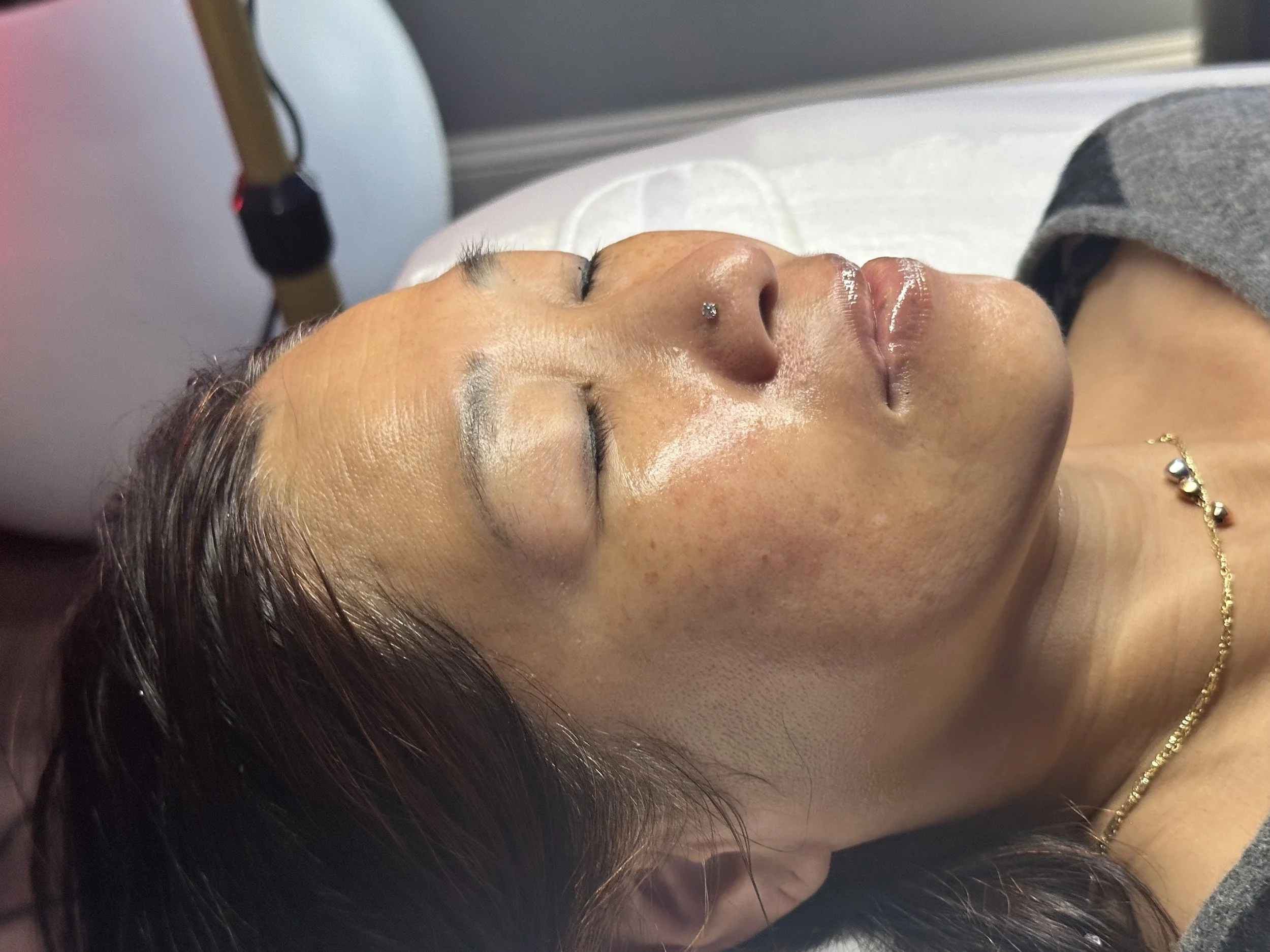 A woman with medium skin tone lying on her back with eyes closed, receiving a facial treatment at Glow Setters Skin Studio, an inclusive skin of color spa located in Jacksonville.