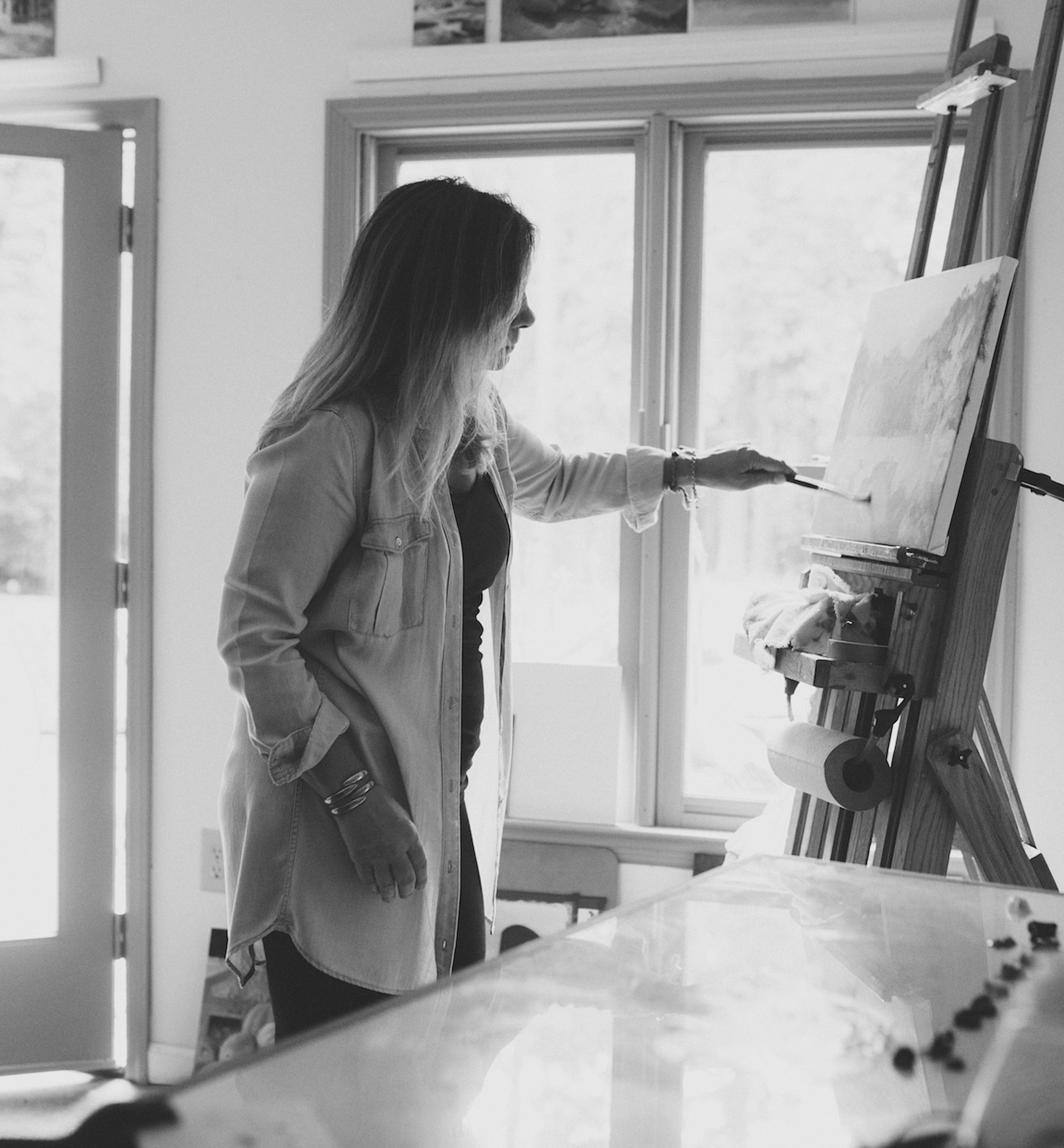 Image of Michaelann Bellerjeau, a woman painting on canvas at an easel inside a brightly lit room.