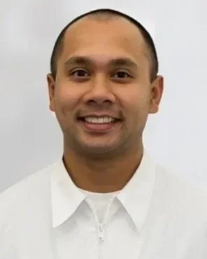 Portrait of a smiling man with short hair, wearing a white shirt, against a plain background.