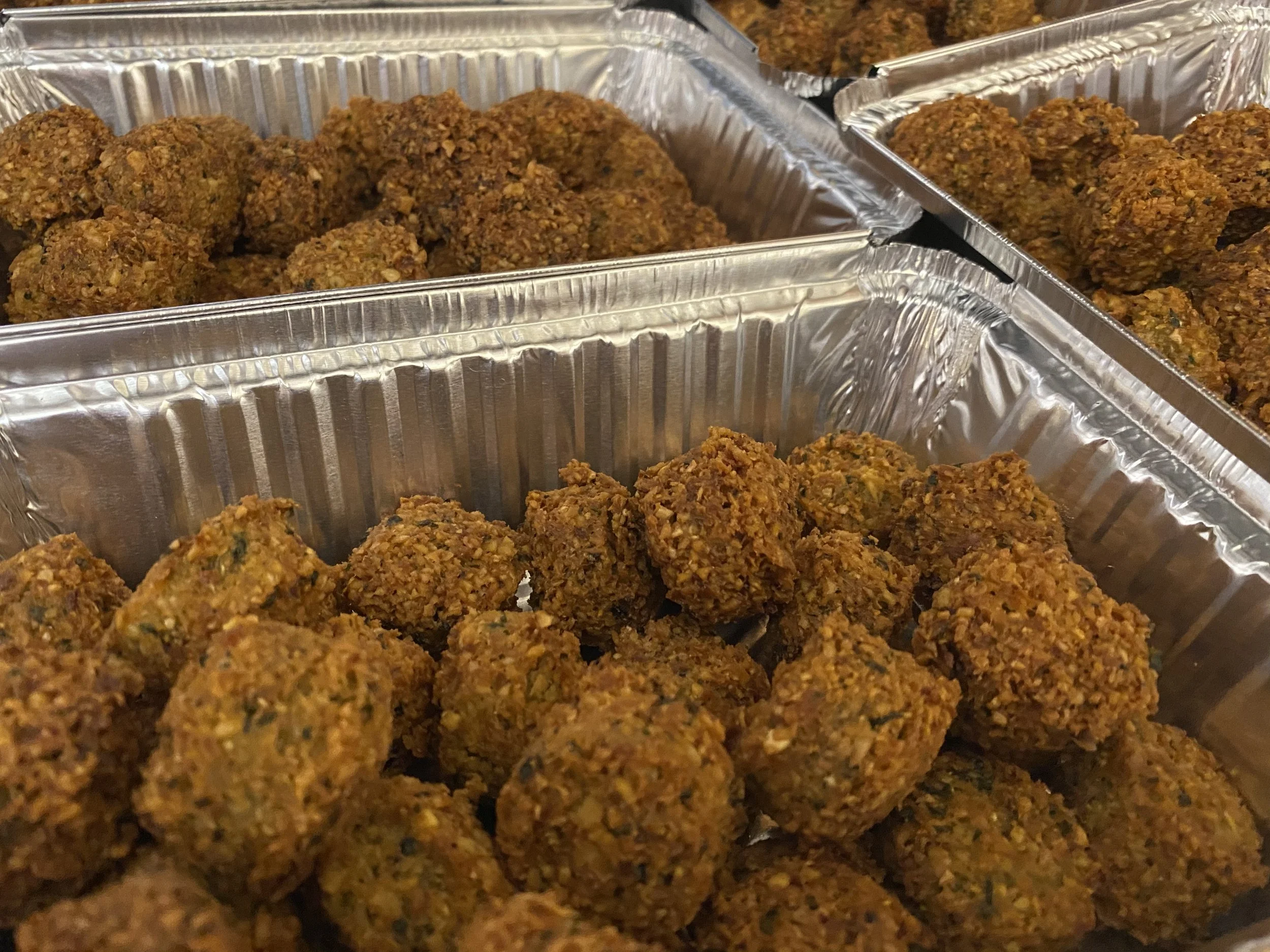 Multiple aluminum trays filled with cooked falafel balls.