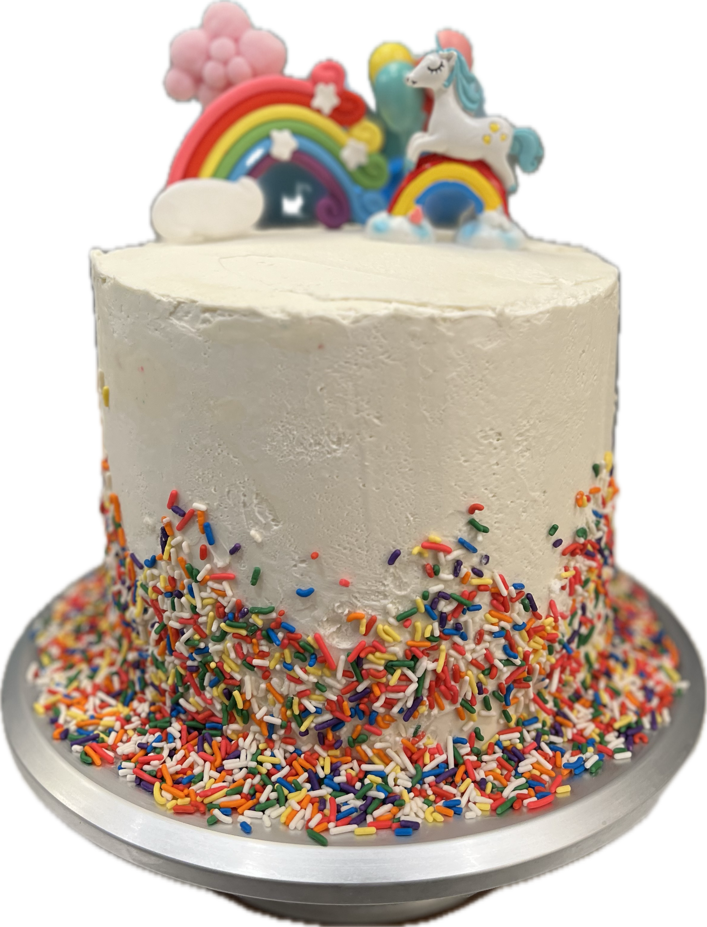 A birthday cake with white icing, colorful rainbow and cloud decorations on top, and rainbow sprinkles around the sides, sitting on a silver tray.