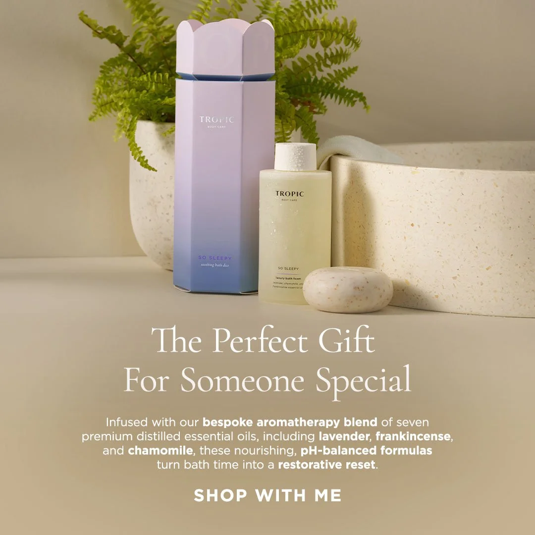 A gift set with bath and body products, including a lavender and blue box, a body foam, and a soap, arranged with a potted fern plant and a speckled stone. The text promotes the products as the perfect gift for someone special, infused with aromather