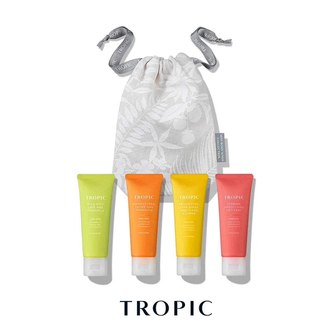 A gift set of four Tropic body wash tubes in lime green, orange, yellow, and pink, placed in front of a white drawstring bag with a gray ribbon and tropical print design.