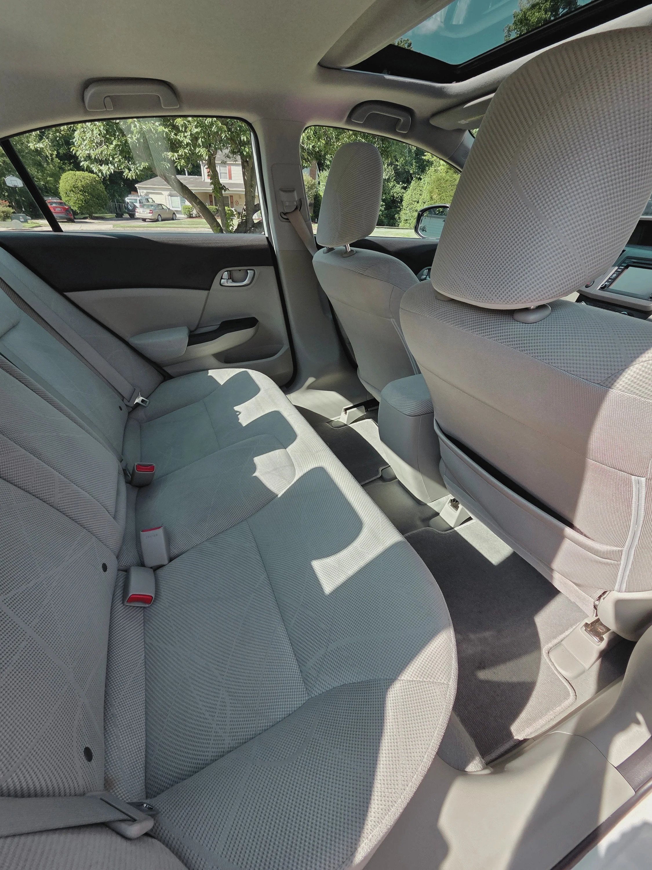 The interior of a car showing the back seat, front seats, and sunroof with trees visible outside.