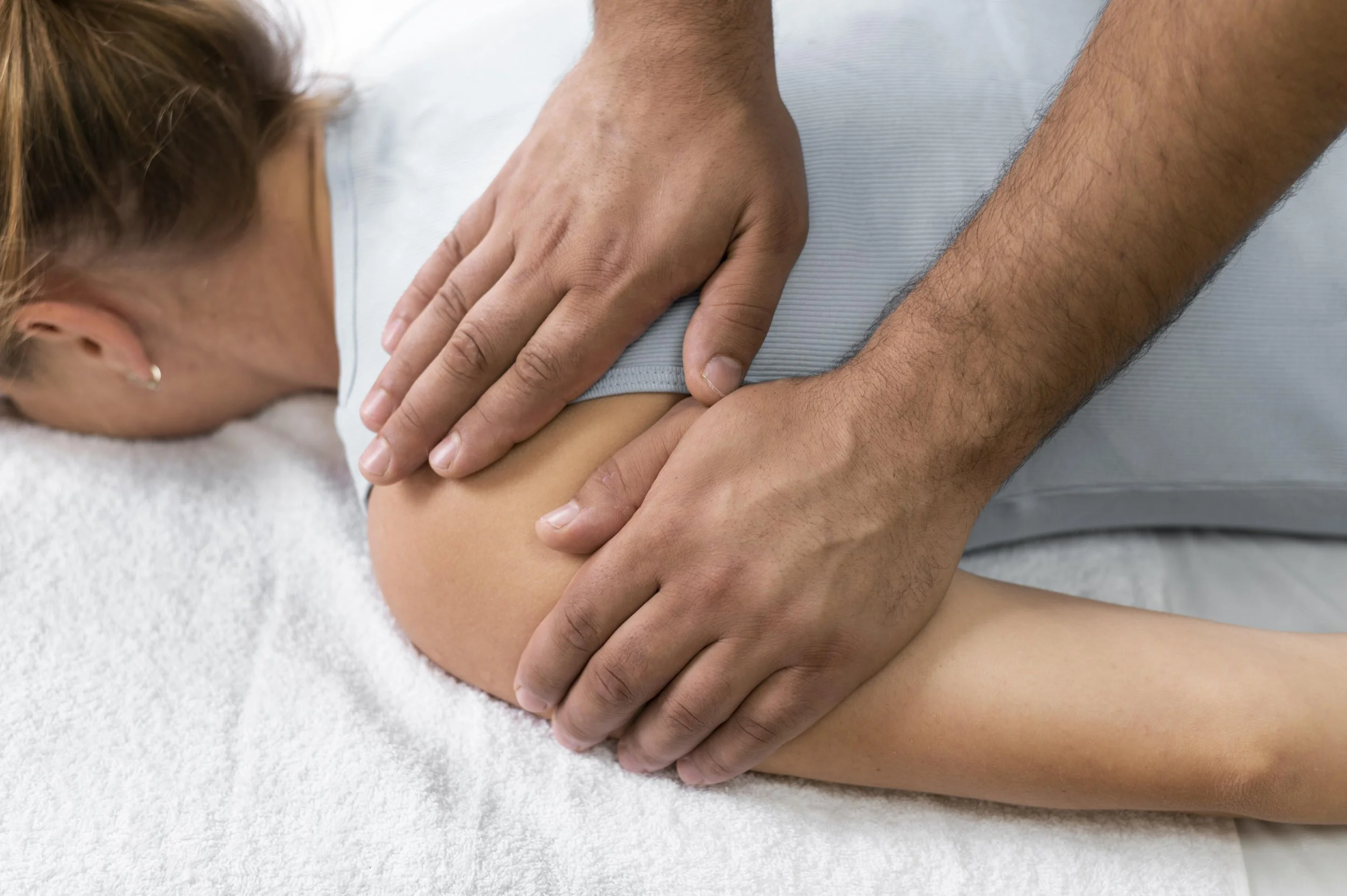 Person receiving a massage on their shoulder while lying face down on a massage table.