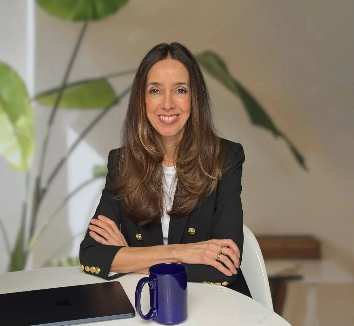 staci perelman wearing a blue blazer and sitting at a white table with bright blue coffee mug