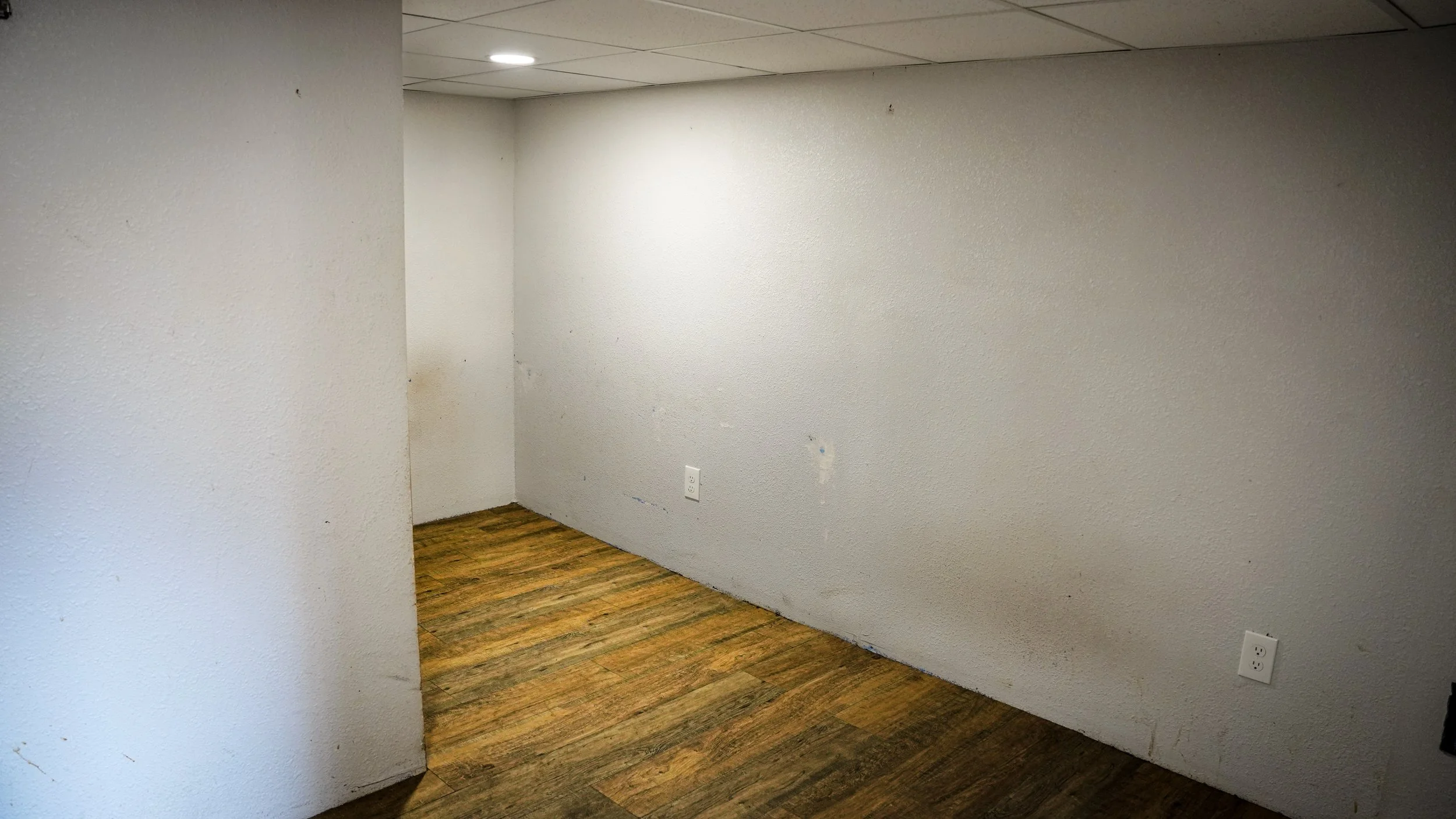 Empty room with white textured walls, brown wood laminate flooring, and two electrical outlets.
