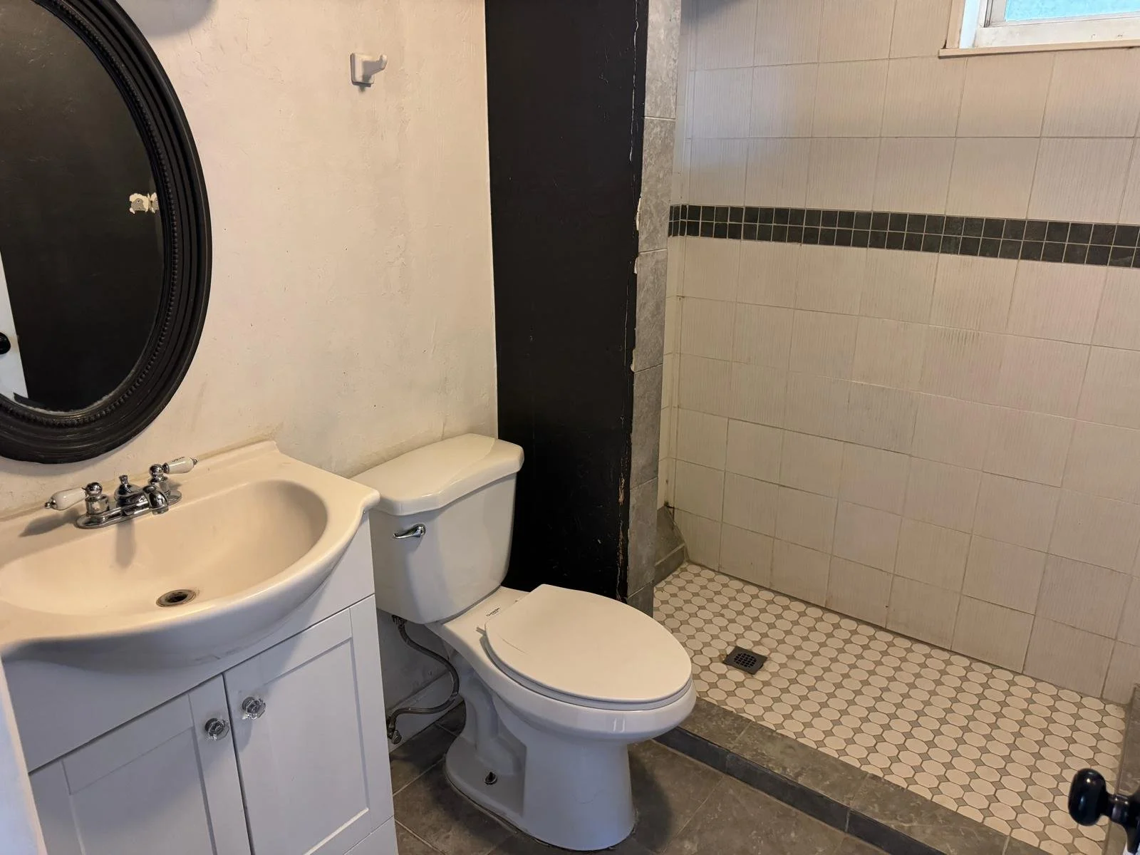 Bathroom with white sink, toilet, and walk-in shower with beige tiles and small hexagonal floor tiles.
