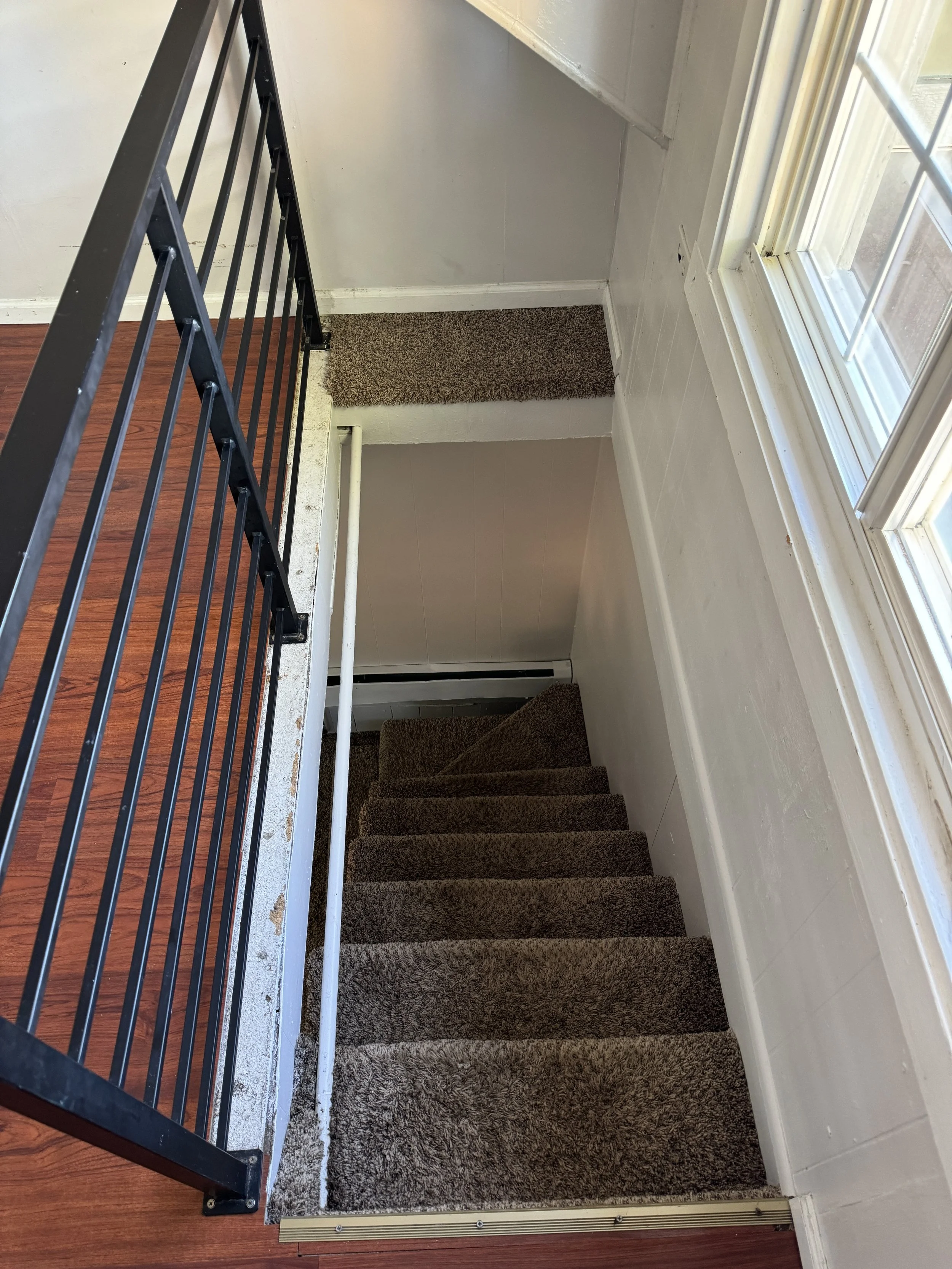 View of staircase with brown carpet, white walls, and a large window allowing natural light in.