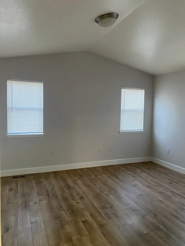 Empty room with two windows, white walls, hardwood floor, and ceiling light fixture.
