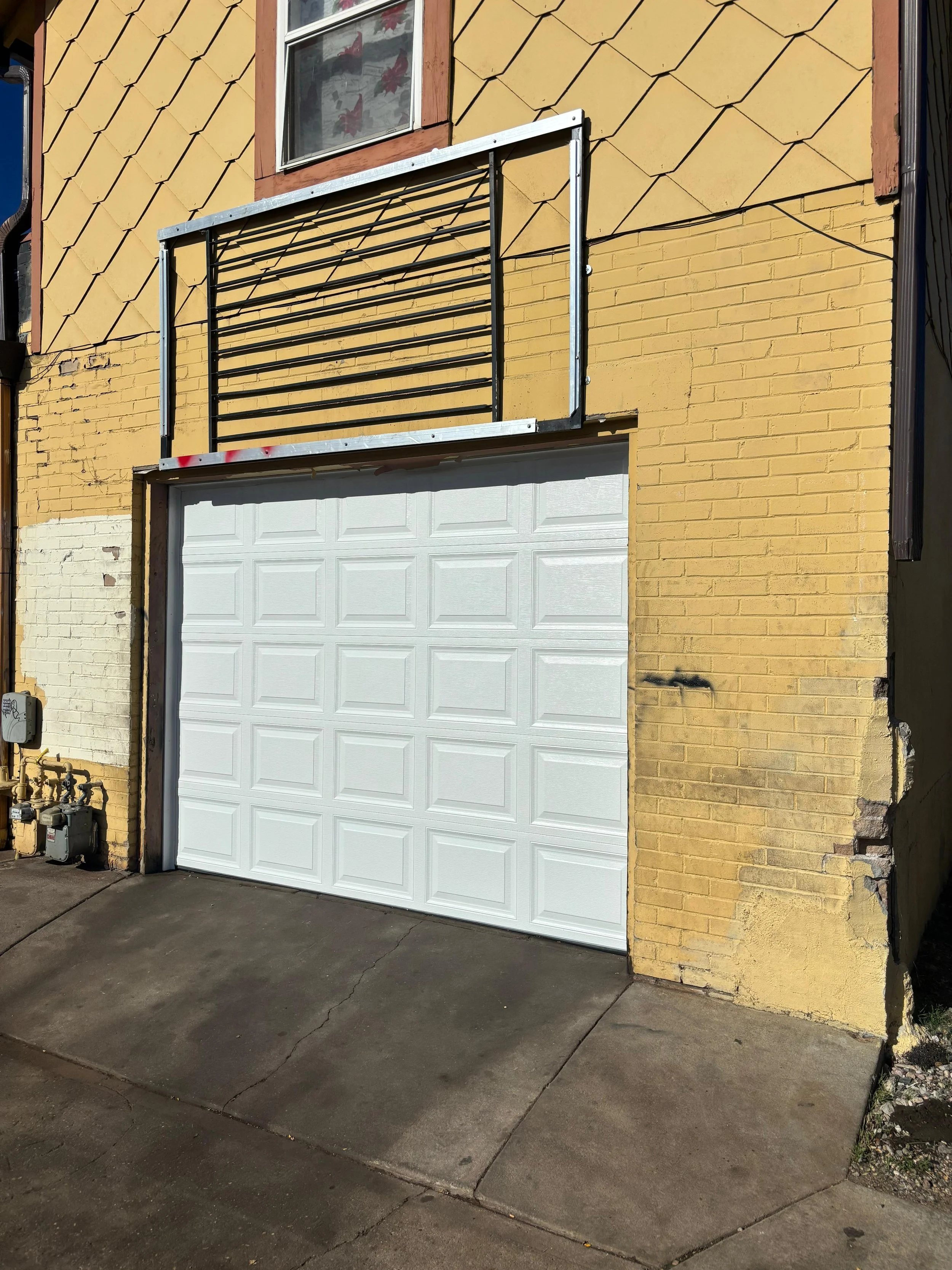 Image of a white garage door, yellow brick building, and a metal frame structure above the garage.