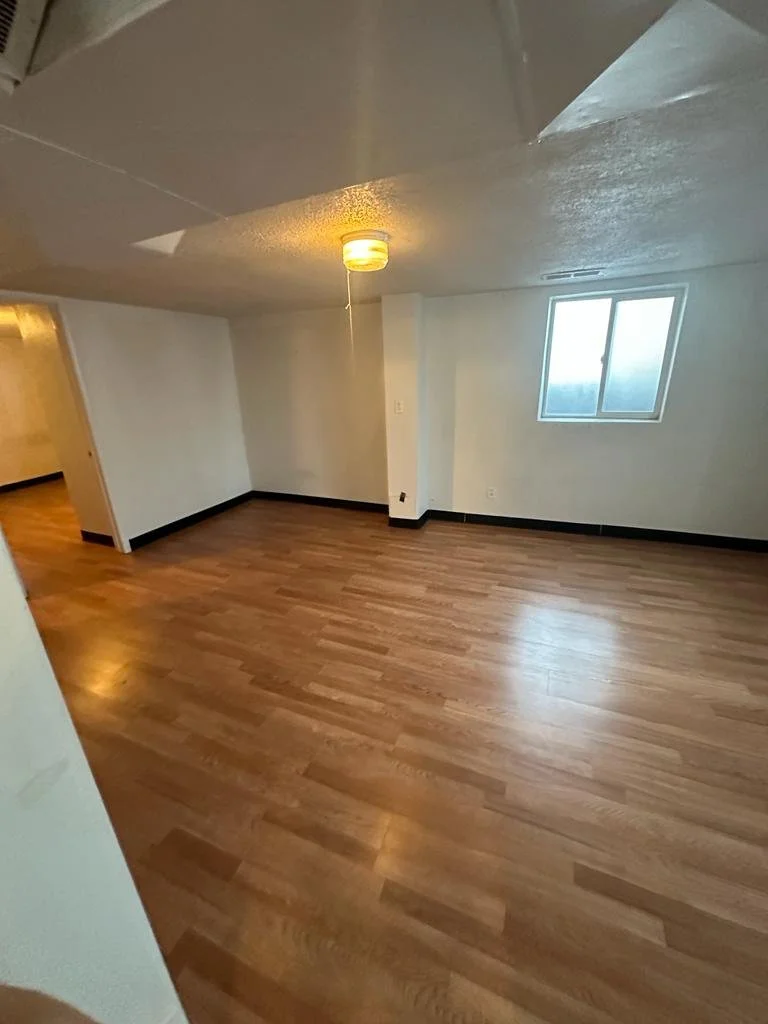 Empty room with wood flooring, white walls, a small window, and a ceiling light fixture.